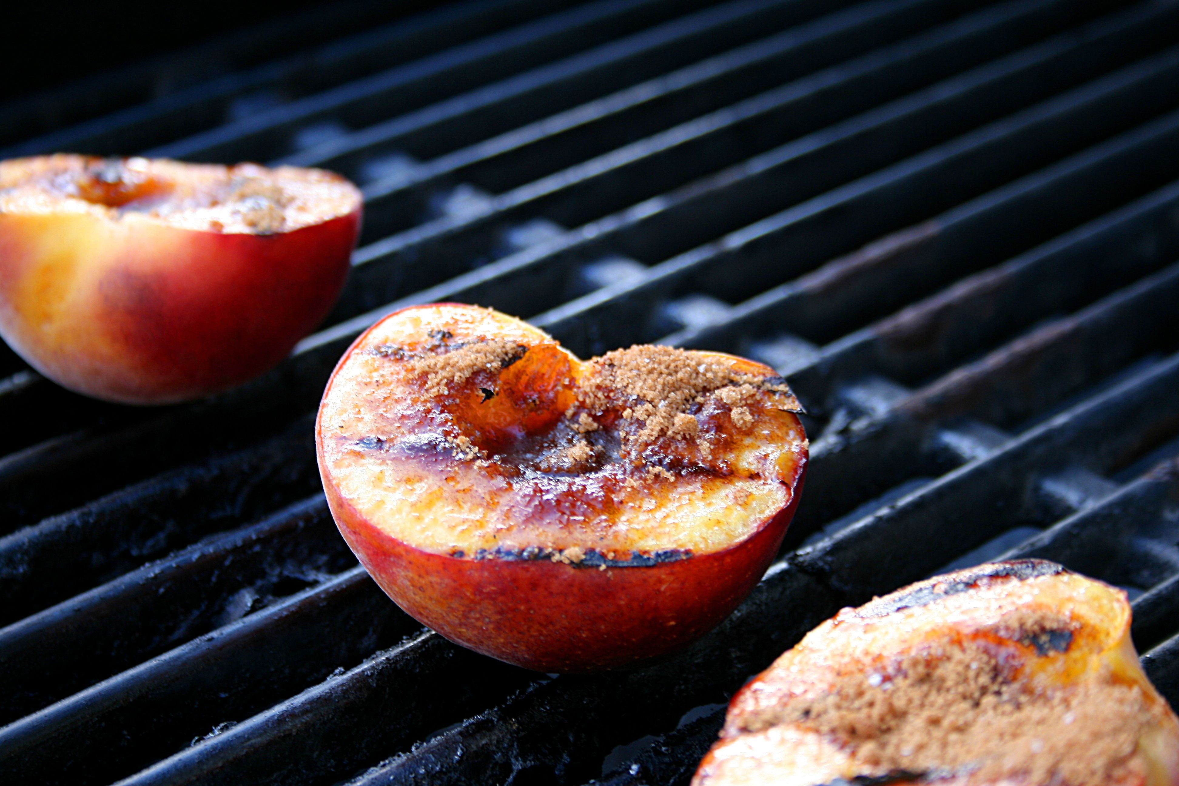 Halbierte Pfirsiche mit braunem Zucker werden auf einem Grillrost gegrillt.