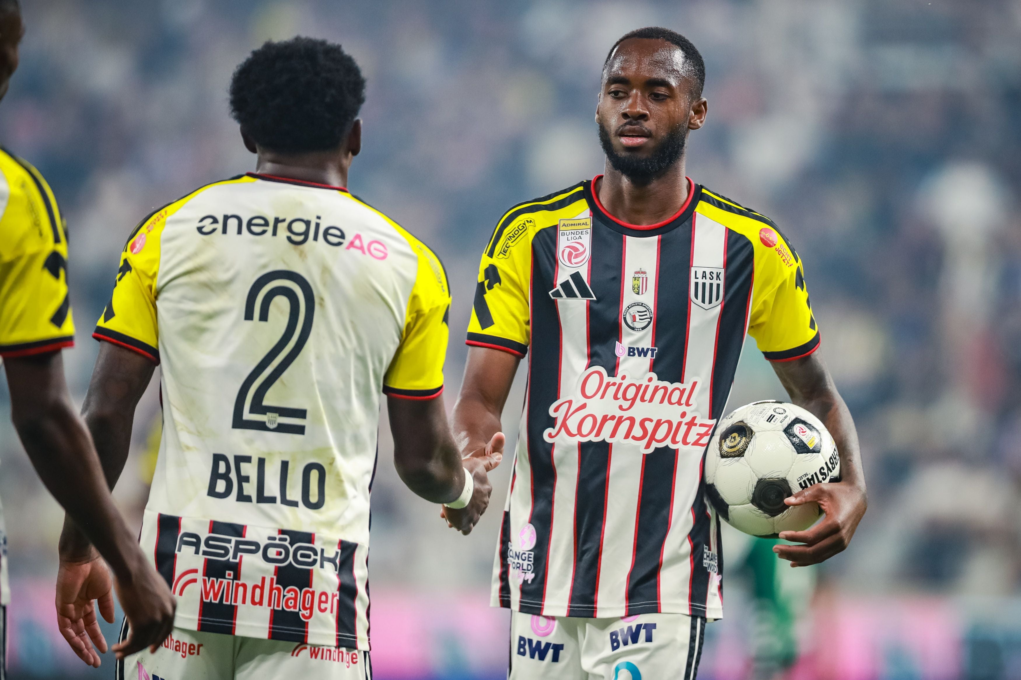 Zwei LASK-Fußballspieler geben sich auf dem Spielfeld die Hand, einer hält einen Ball.