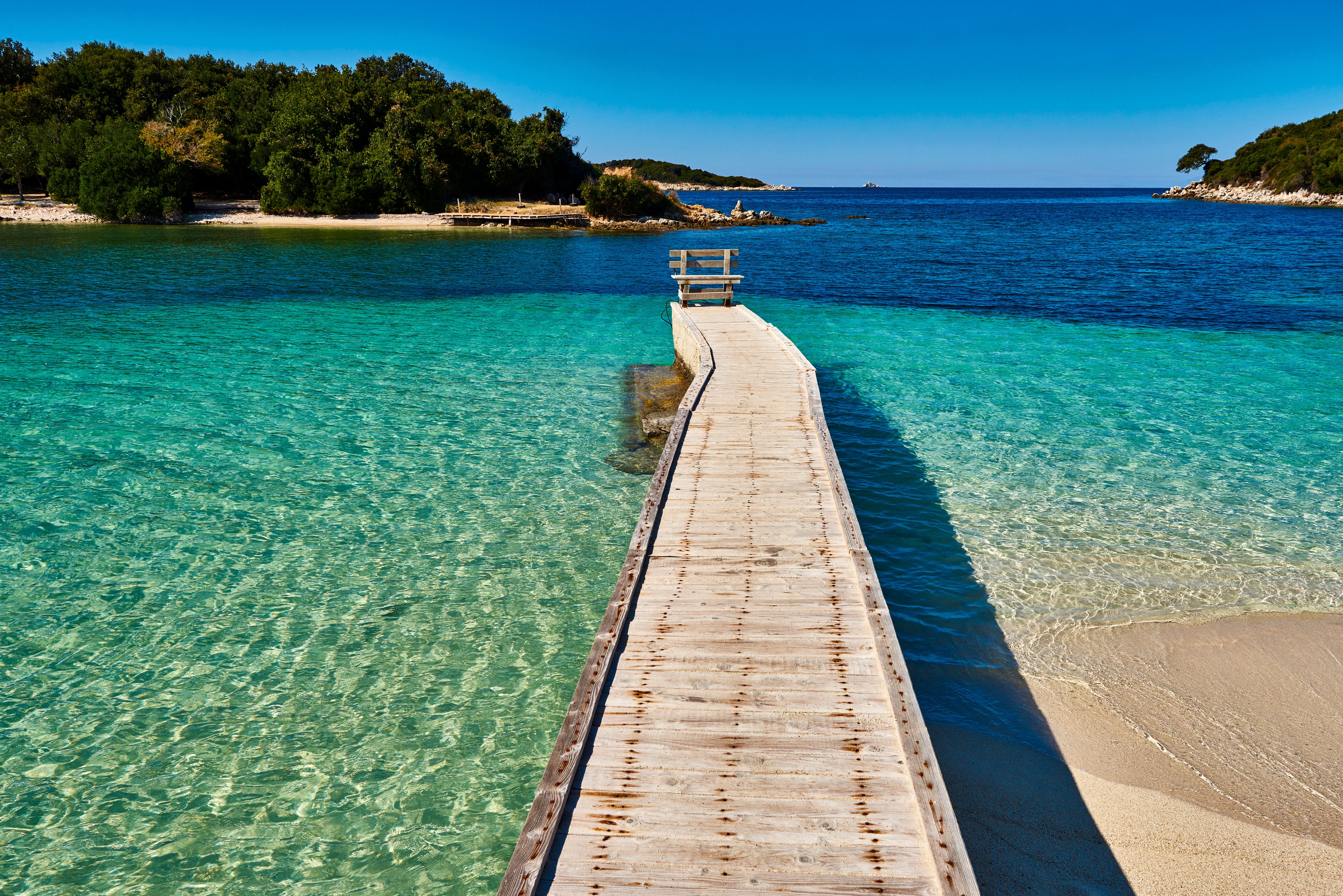 Holzsteg führt über türkisblaues, klares Wasser zum Strand von Ksamil bei Saranda, Albanien.