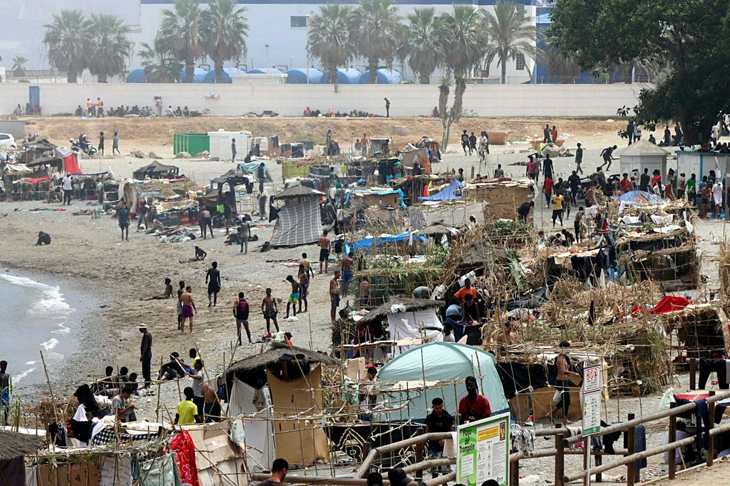 Viele Menschen und provisorische Hütten an einem Strand in Ceuta, Spanien.