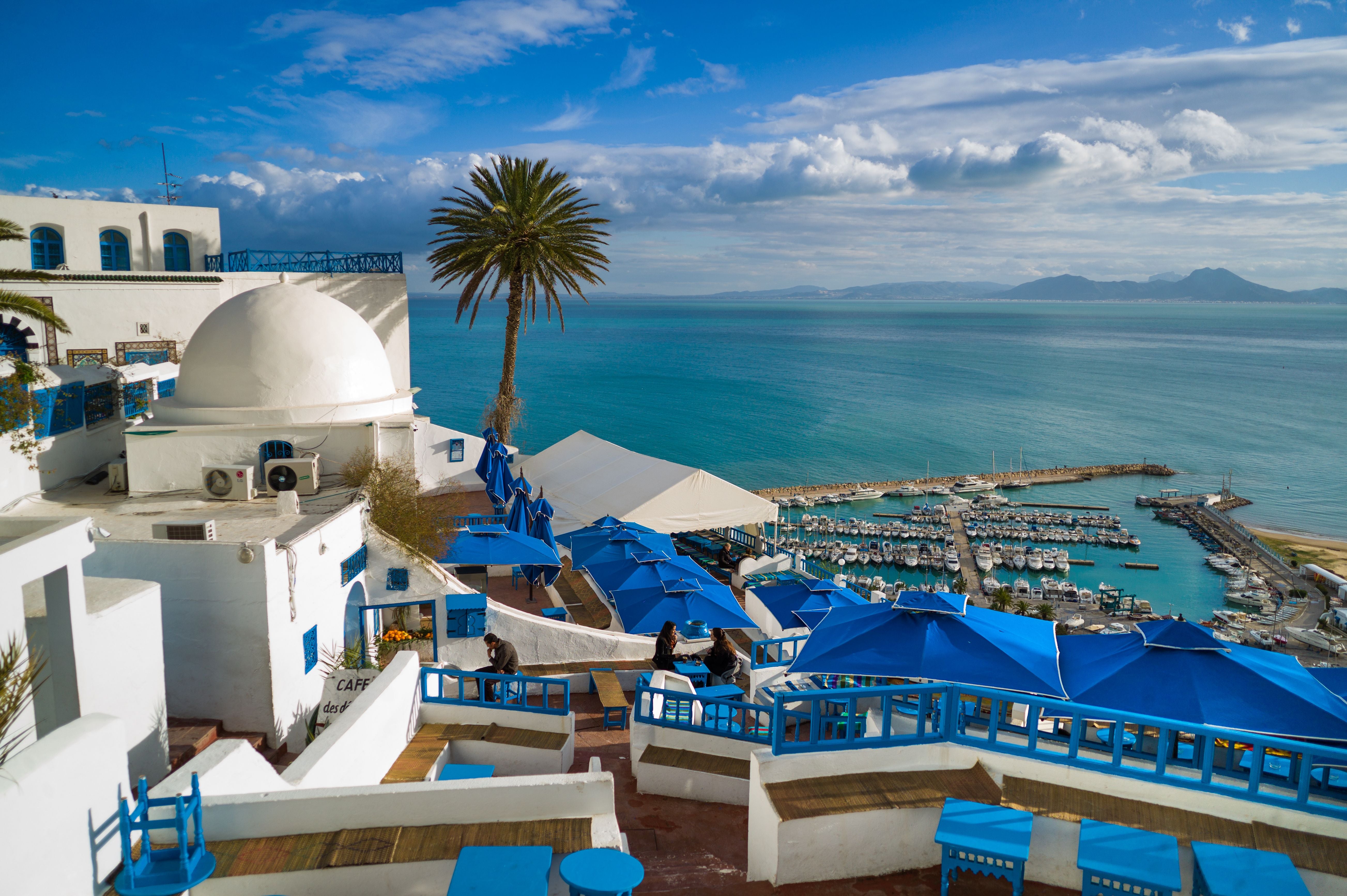 Blick auf ein weiß-blaues Café mit Meerblick und Yachthafen in Sidi Bou Said, Tunesien.