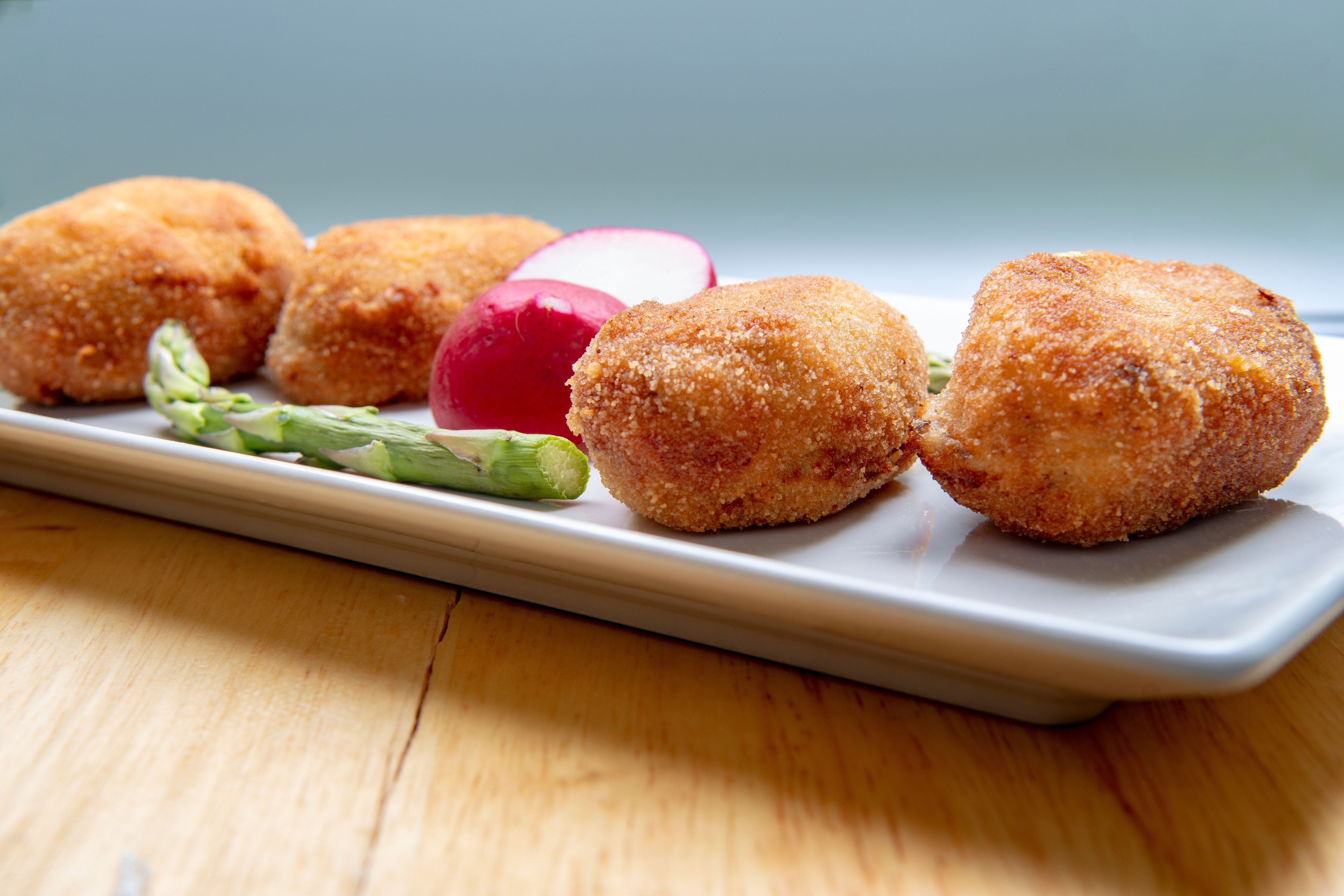 Vier panierte Kroketten mit Spargel und Radieschen auf einem weißen Teller.