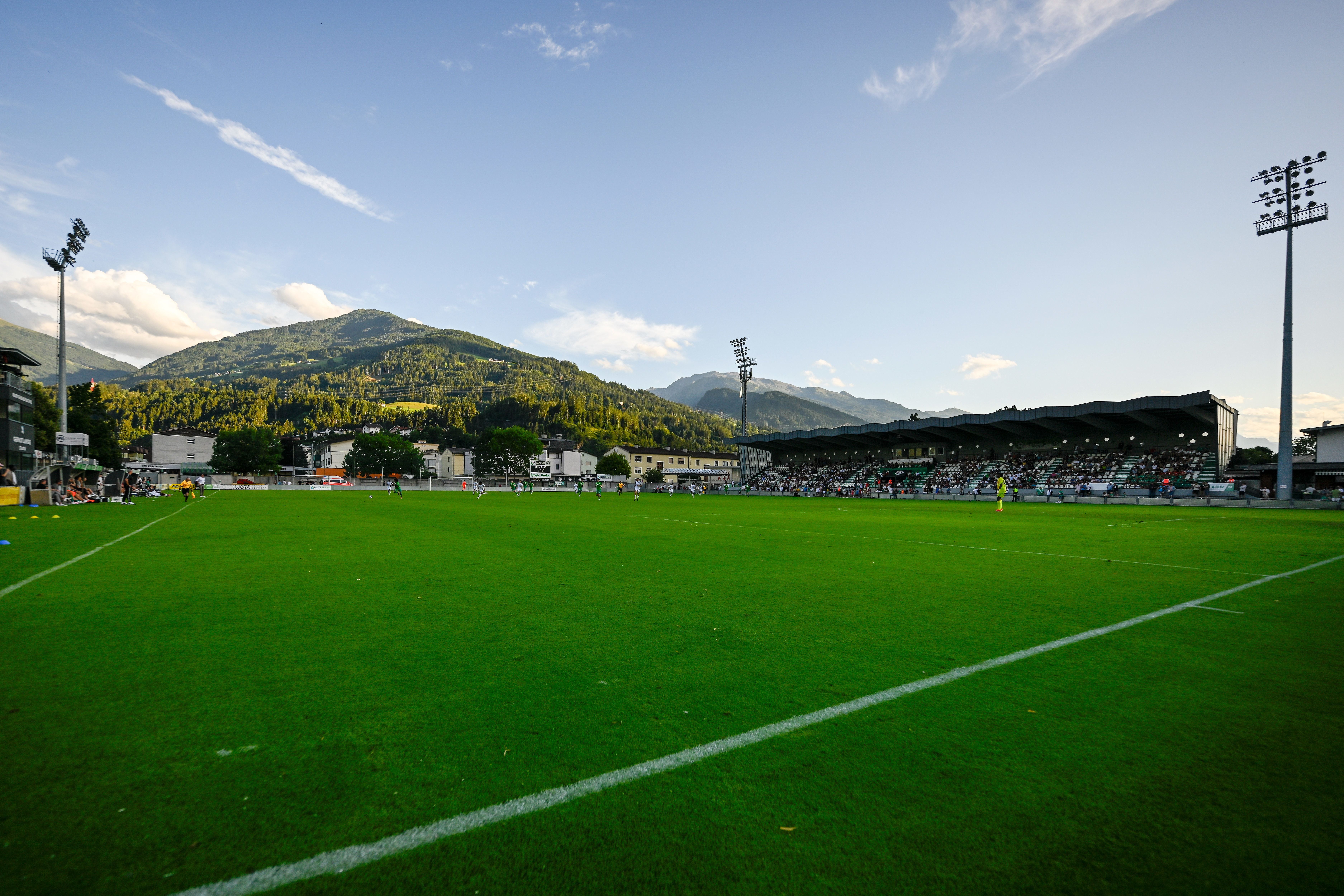 Fußballstadion in Wattens mit grünen Tribünen und Bergen im Hintergrund bei Tageslicht.