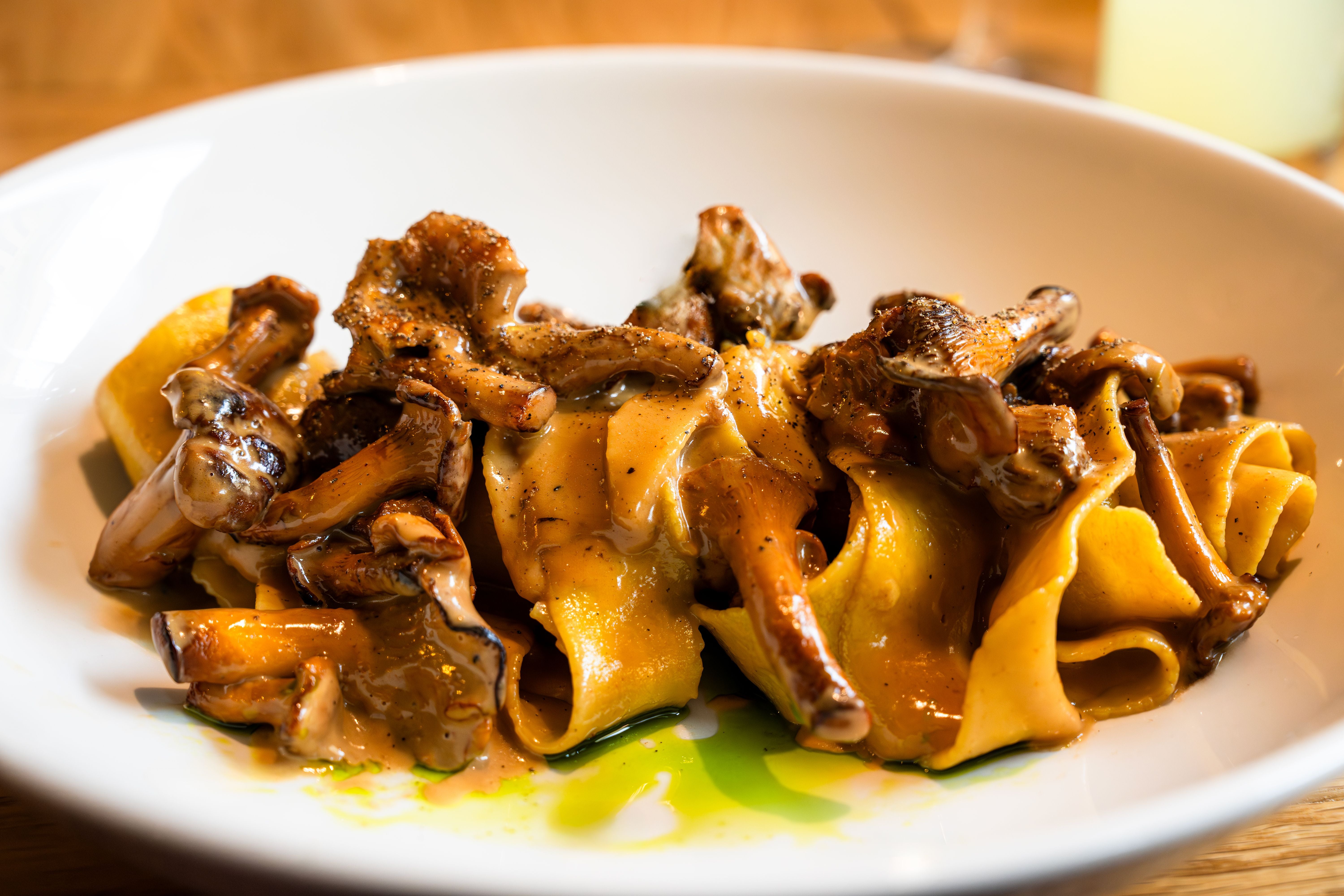 Pappardelle mit Pfifferlingen in cremiger Sauce und Olivenöl auf weißem Teller serviert.