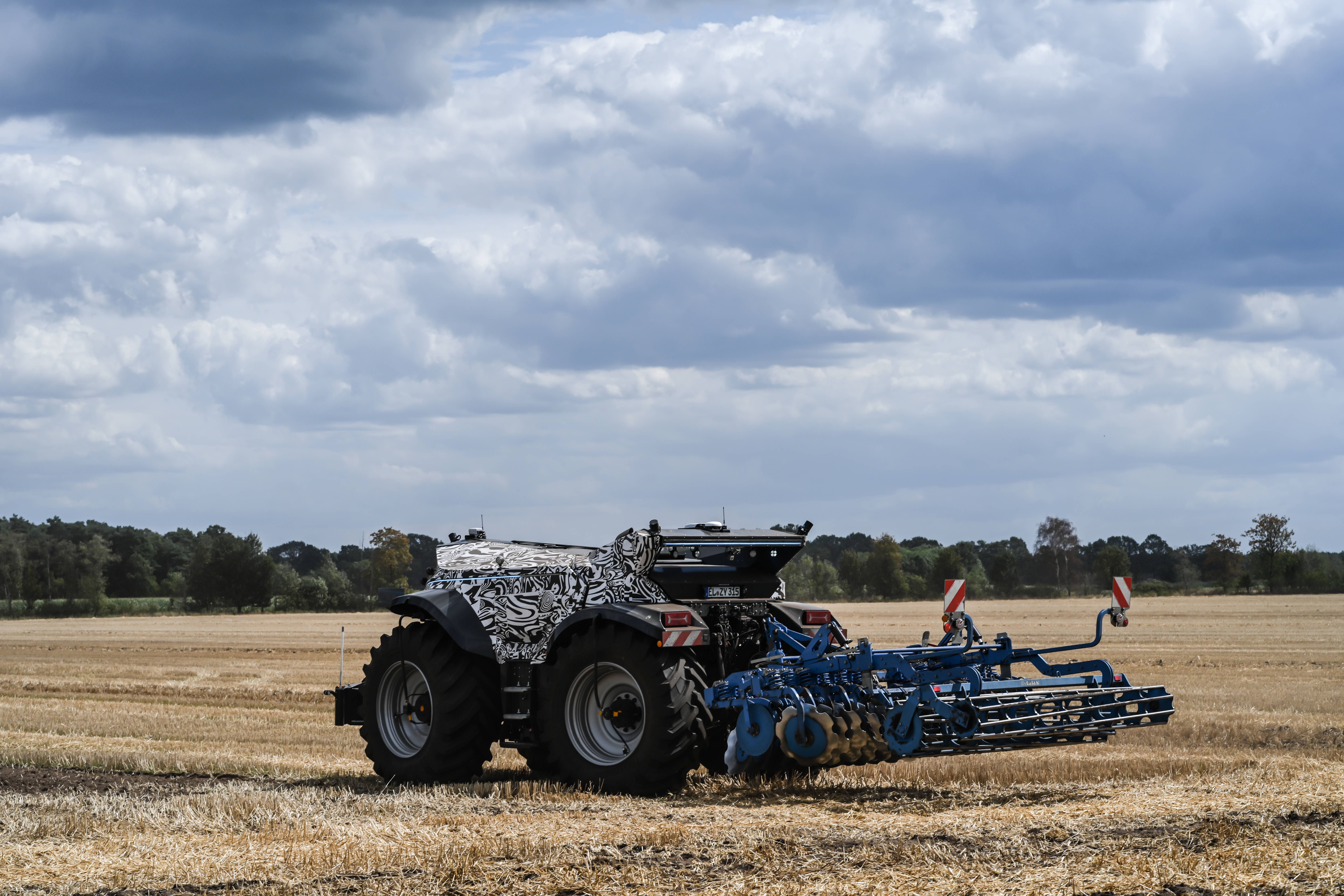 Autonomer, fahrerkabinenloser Traktor arbeitet mit Anbaugerät auf einem abgeernteten Feld.