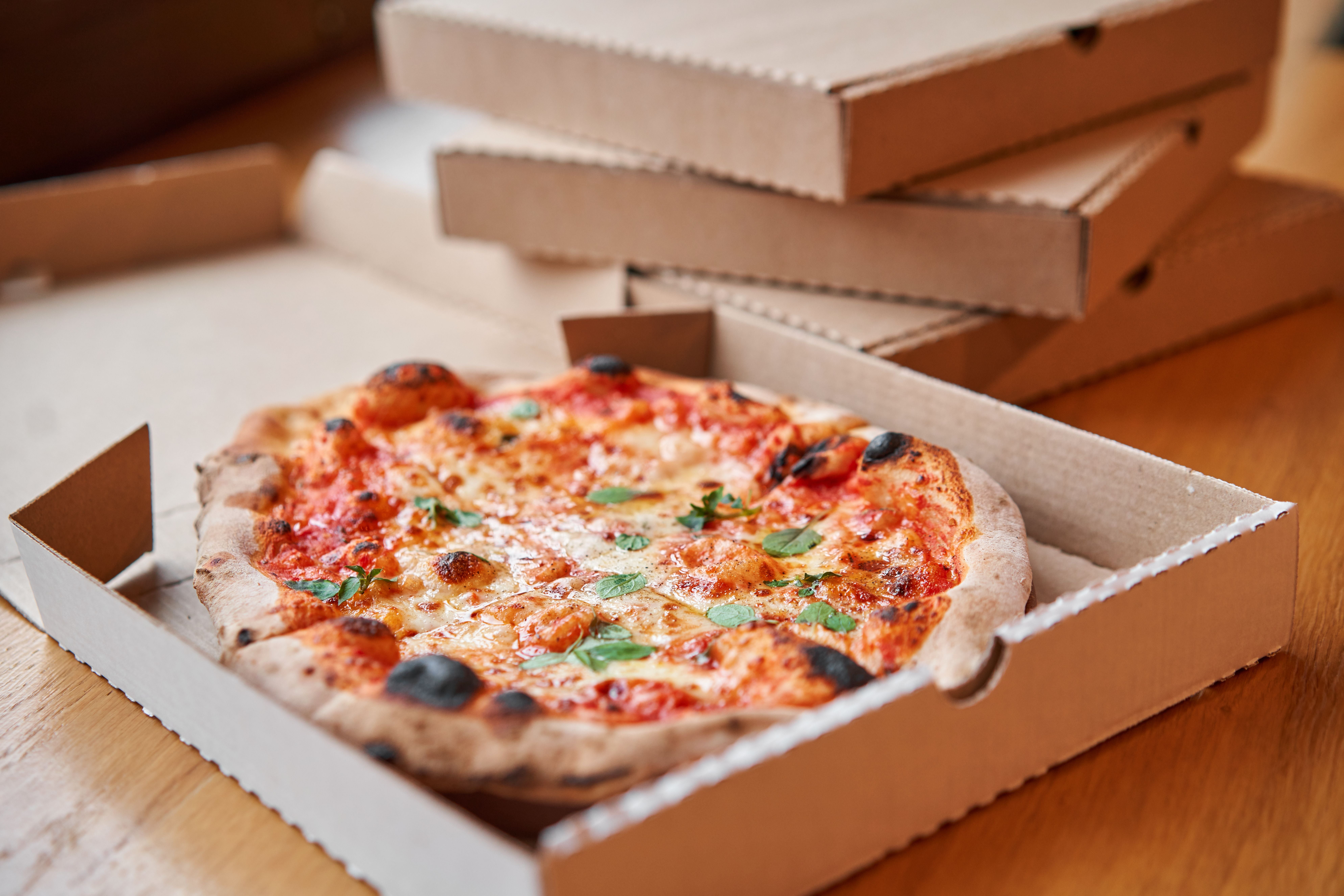 Frische Margherita-Pizza liegt in einem offenen Pizzakarton auf einem Holztisch.