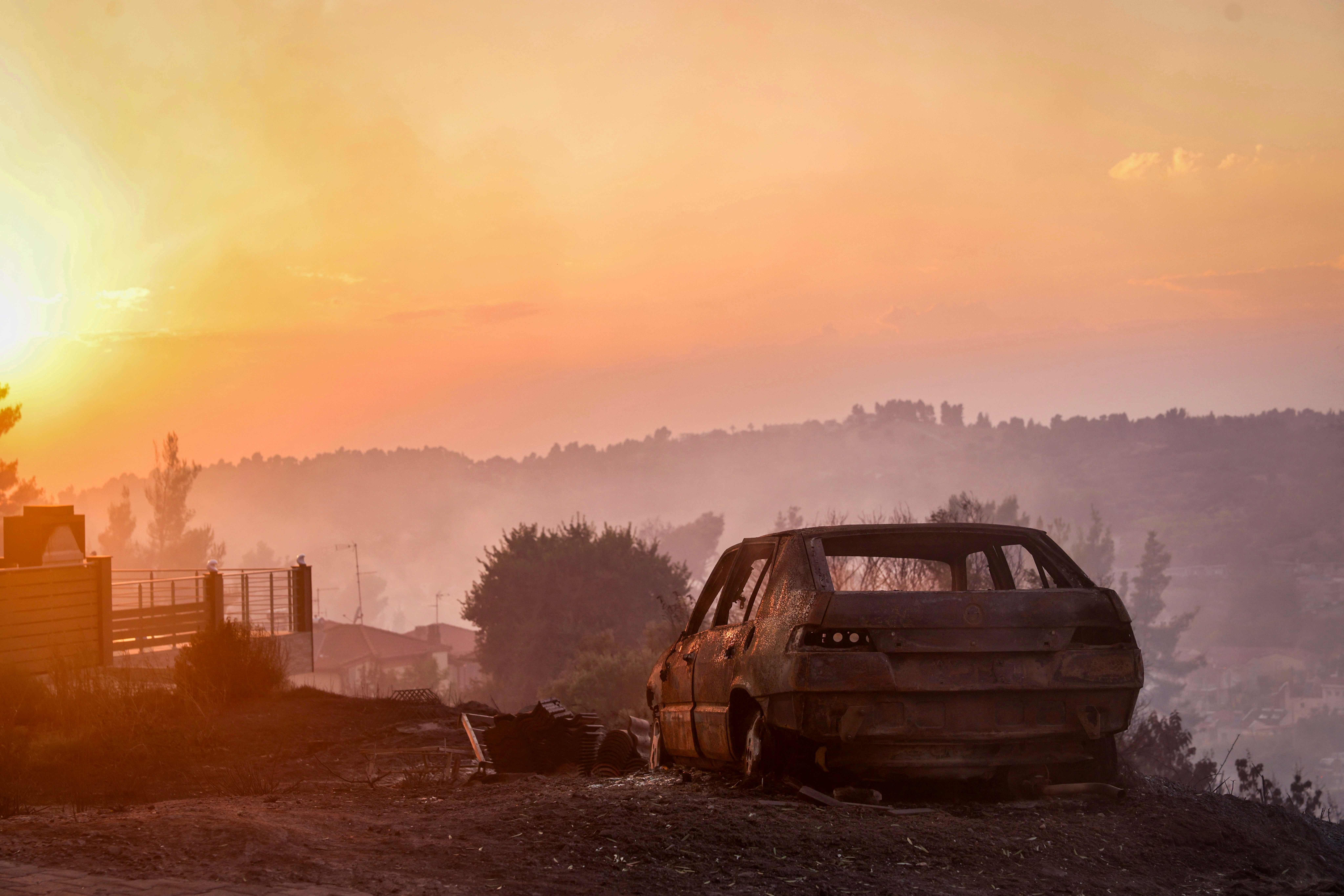 Ausgebranntes Auto auf einem Hügel bei Sonnenuntergang nach einem Waldbrand in Nordgriechenland.