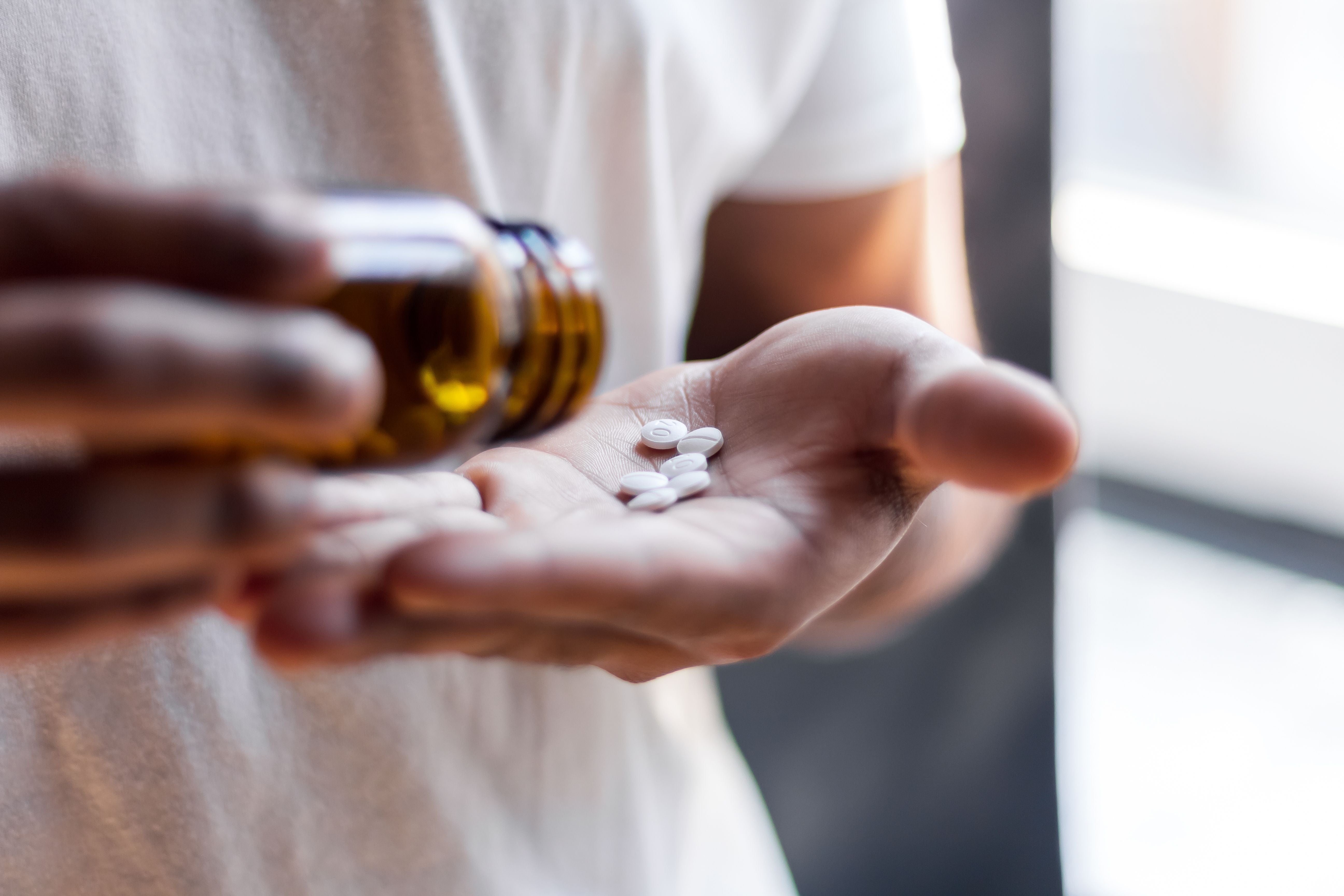 Eine Person kippt weiße Tabletten aus einer braunen Flasche in ihre Hand.