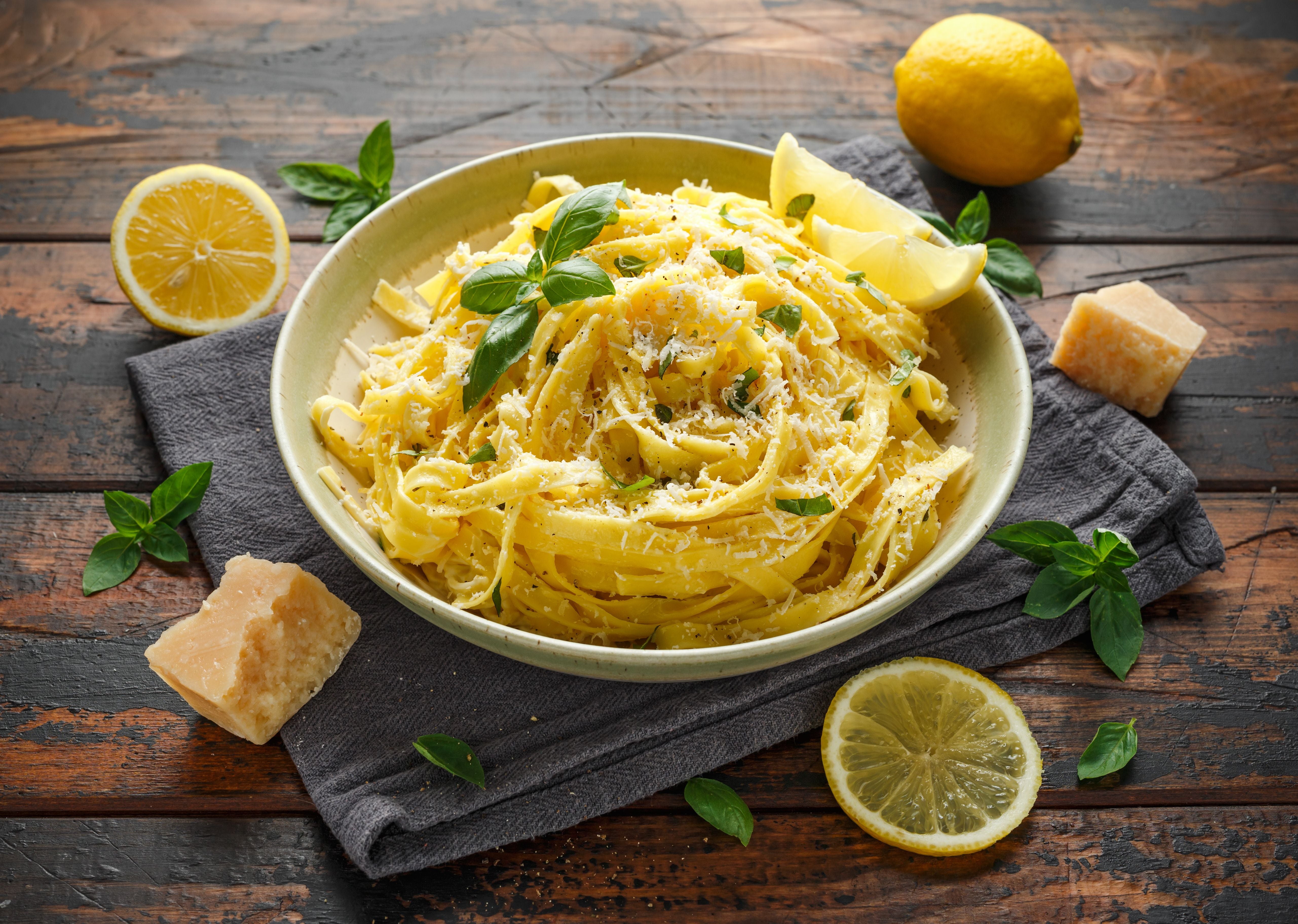 Tagliatelle mit Zitronenscheiben, Basilikum und geriebenem Parmesan auf einem rustikalen Holztisch.