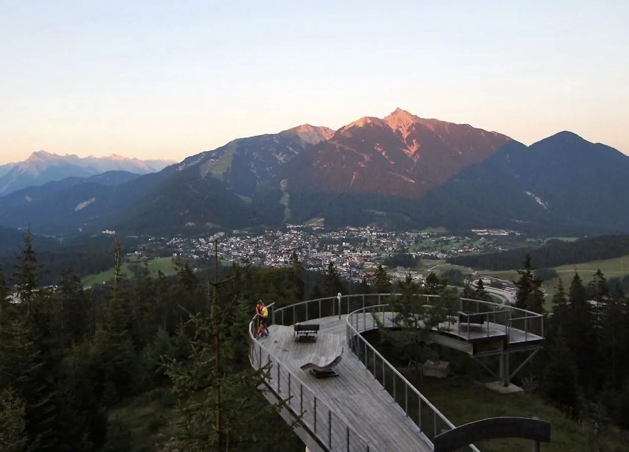 Aussichtsplattform im Wald mit Blick auf ein Tal und Berge im Sonnenuntergang.