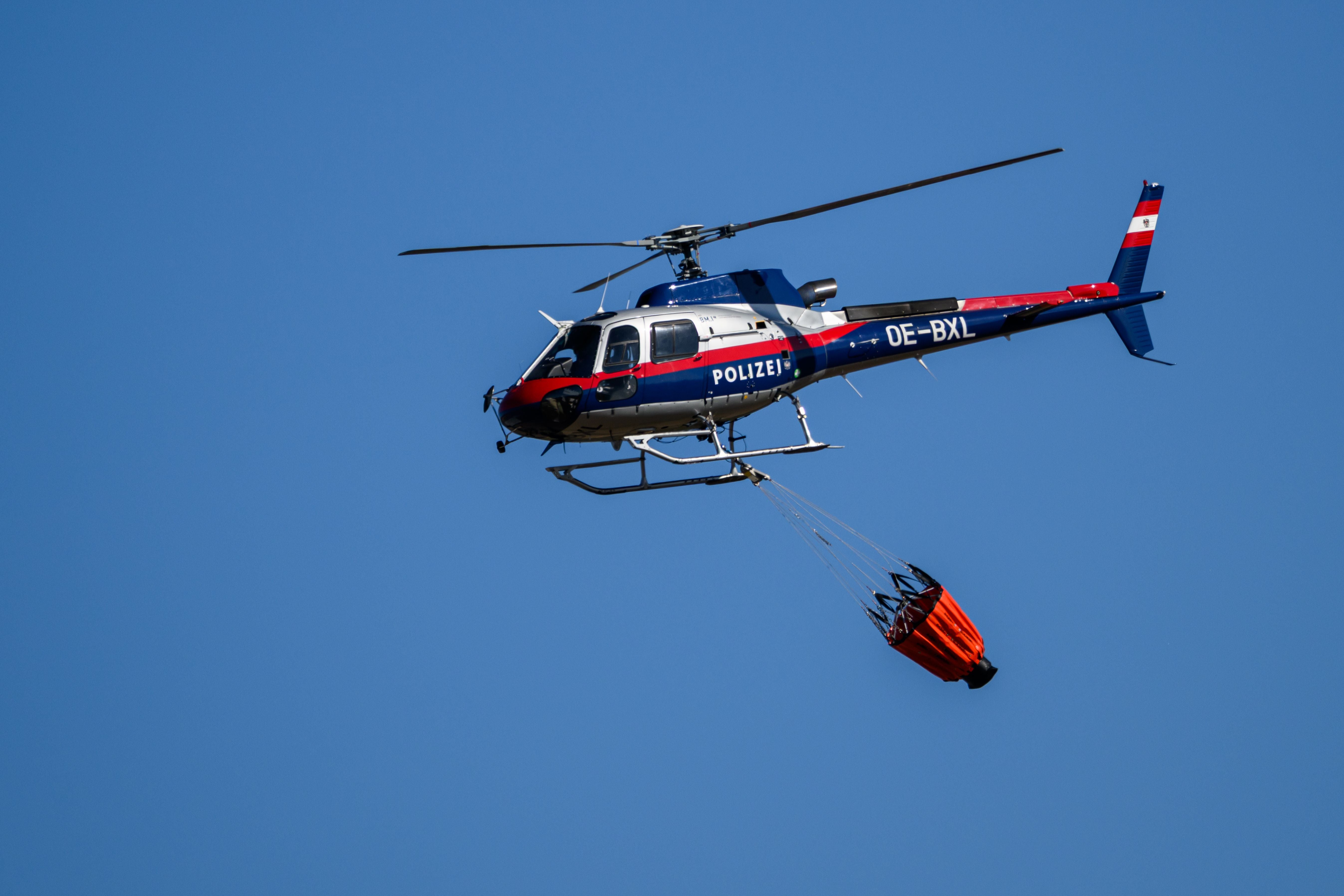 Ein BMI-Polizeihubschrauber fliegt mit Löschbehälter.