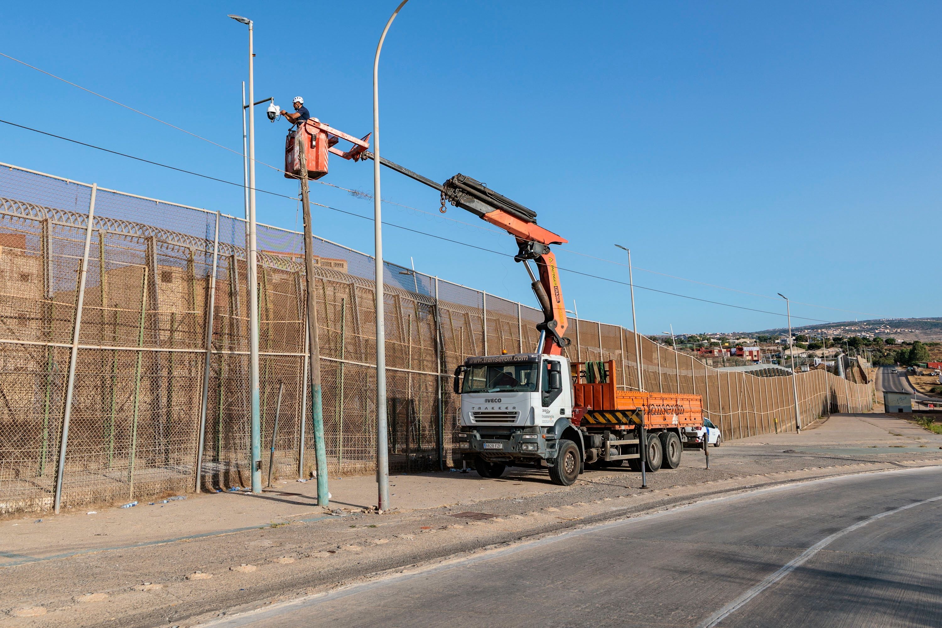 Ein Arbeiter verstärkt mit einem Kran die Grenzsicherung an einem hohen Zaun in Melilla, Spanien.