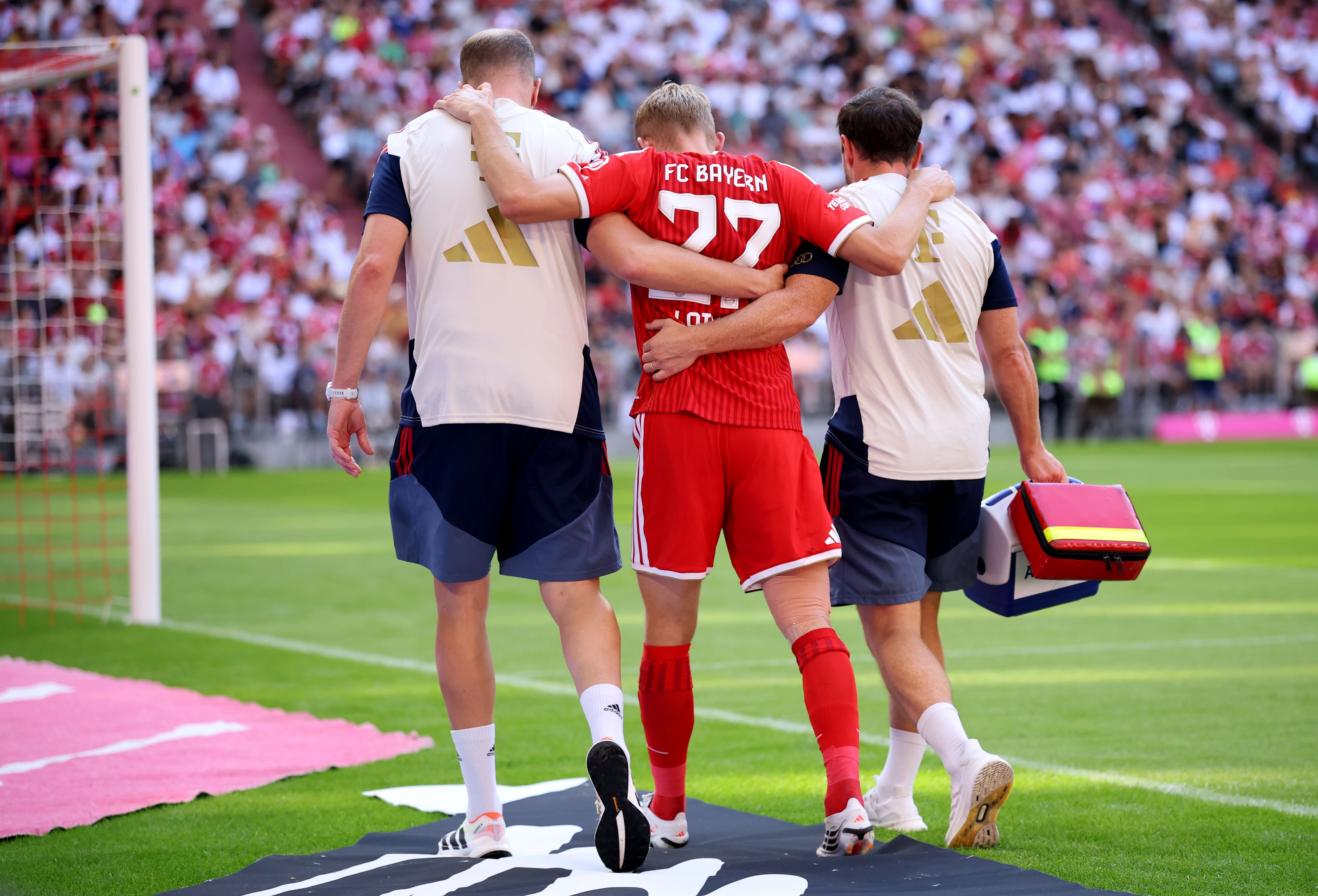 Ein verletzter Bayern-Spieler wird von zwei Medizinern vom Spielfeld geführt.
