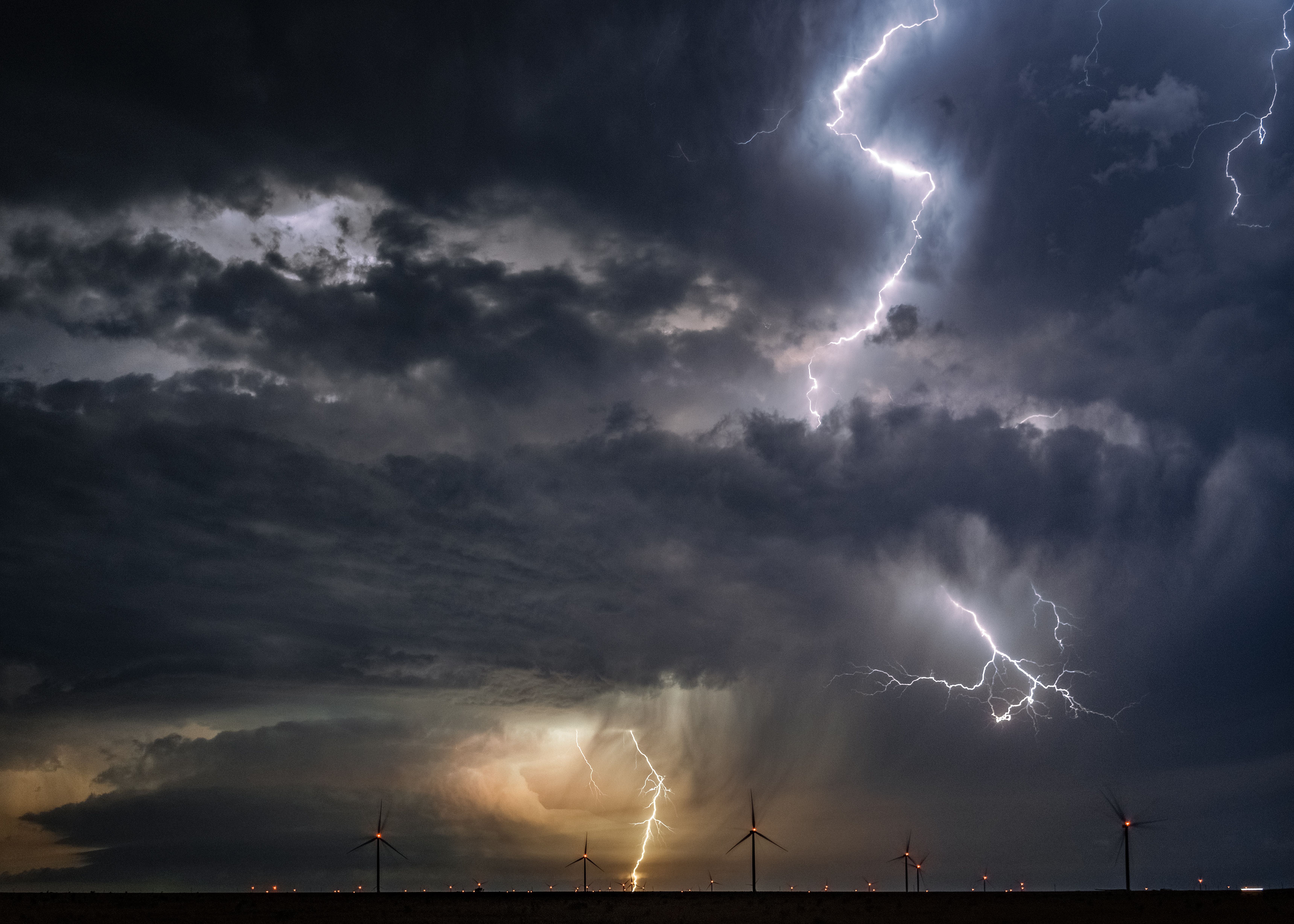 Blitze zucken durch einen dunklen Himmel über Windrädern während eines Superzellengewitters.