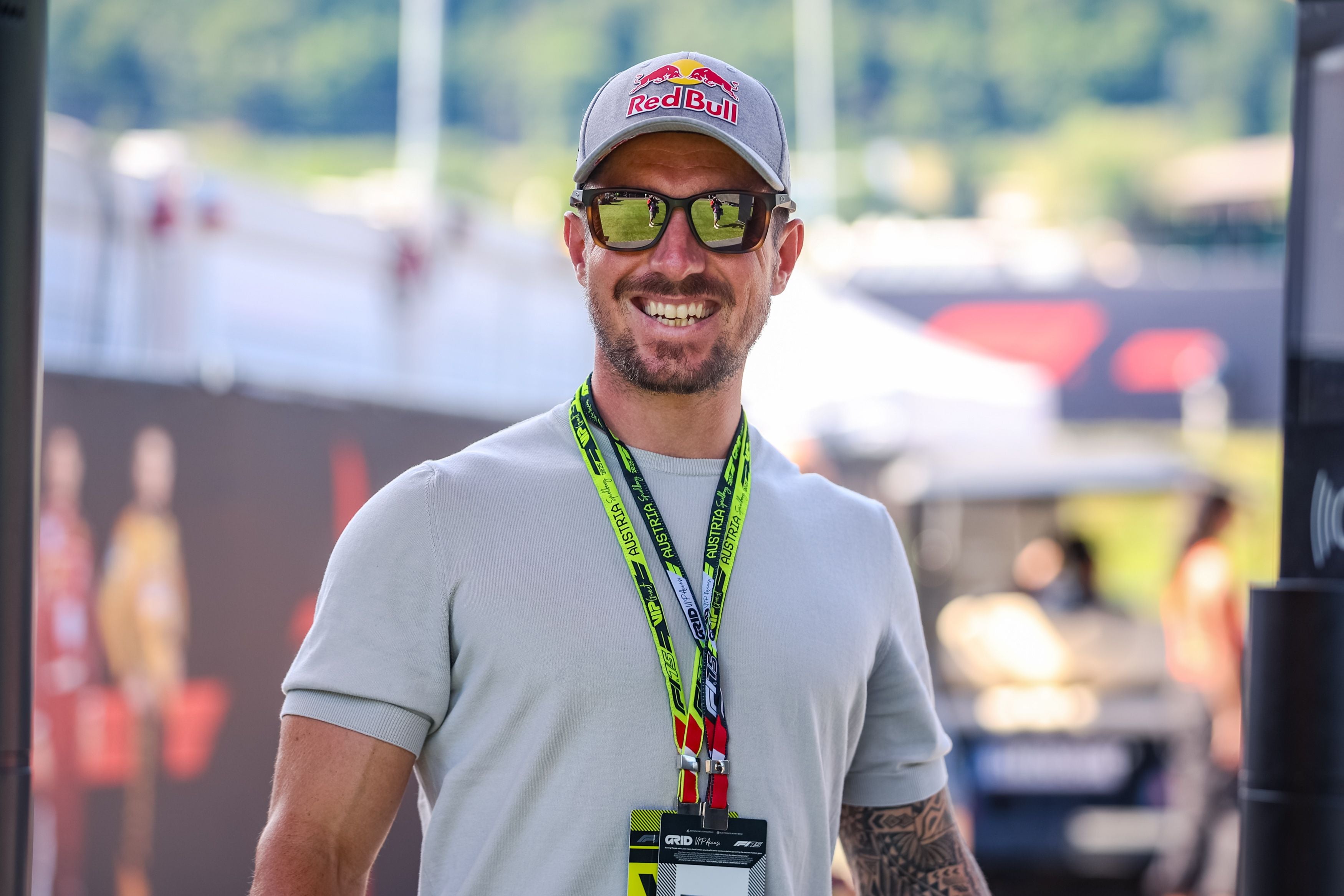 Ein Mann mit Red Bull Kappe und Sonnenbrille lächelt vor dem Formel-1-Paddock in Spielberg.