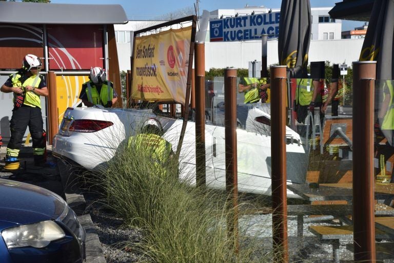 Feuerwehrleute sichern ein weißes Auto, das in einen Gastgarten gefahren ist.