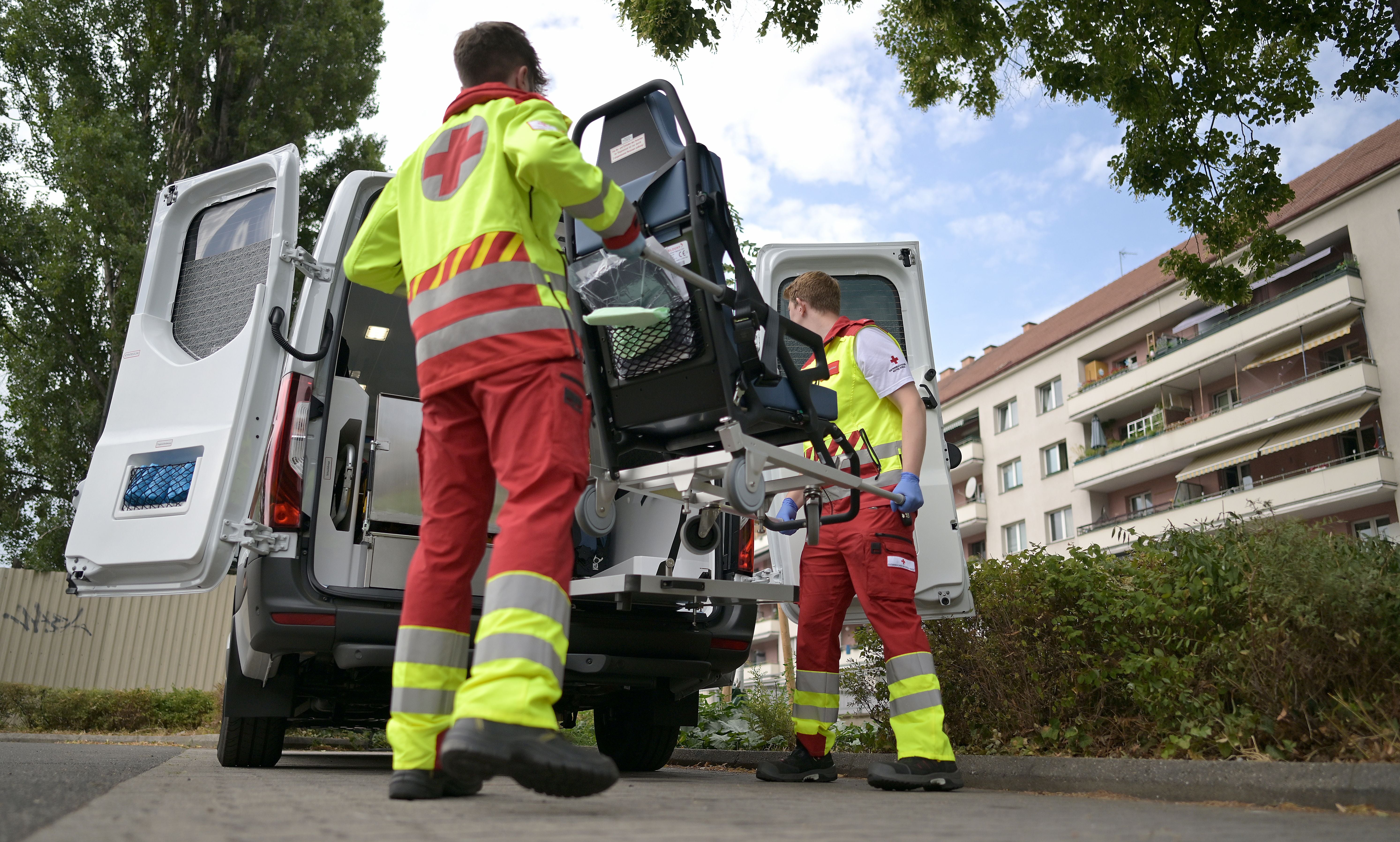 Zwei Sanitäter verladen einen Rettungsstuhl in einen Krankenwagen vor einem Wohnhaus.
