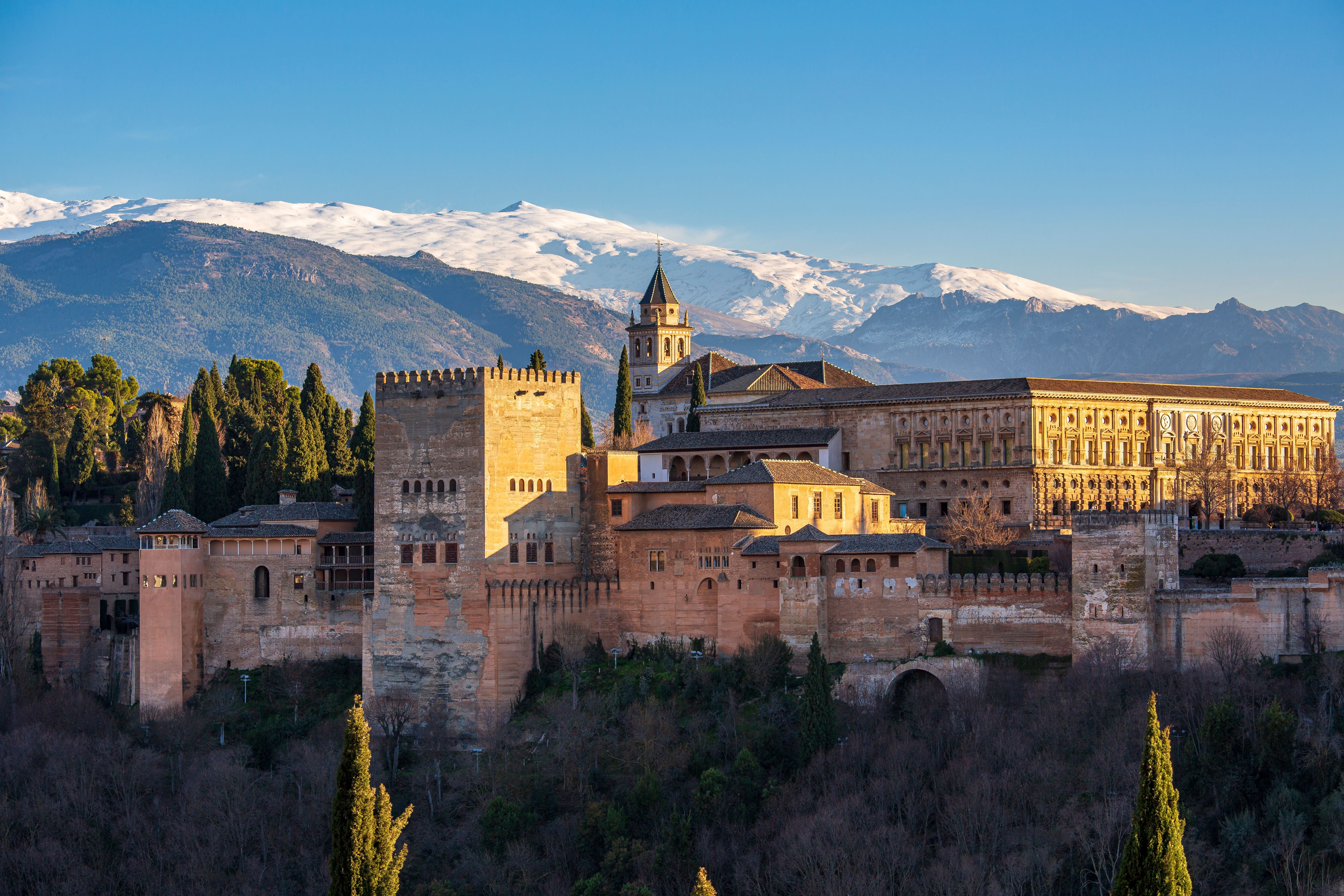 Die Alhambra in Granada vor verschneiten Bergen und klarem, blauem Himmel.