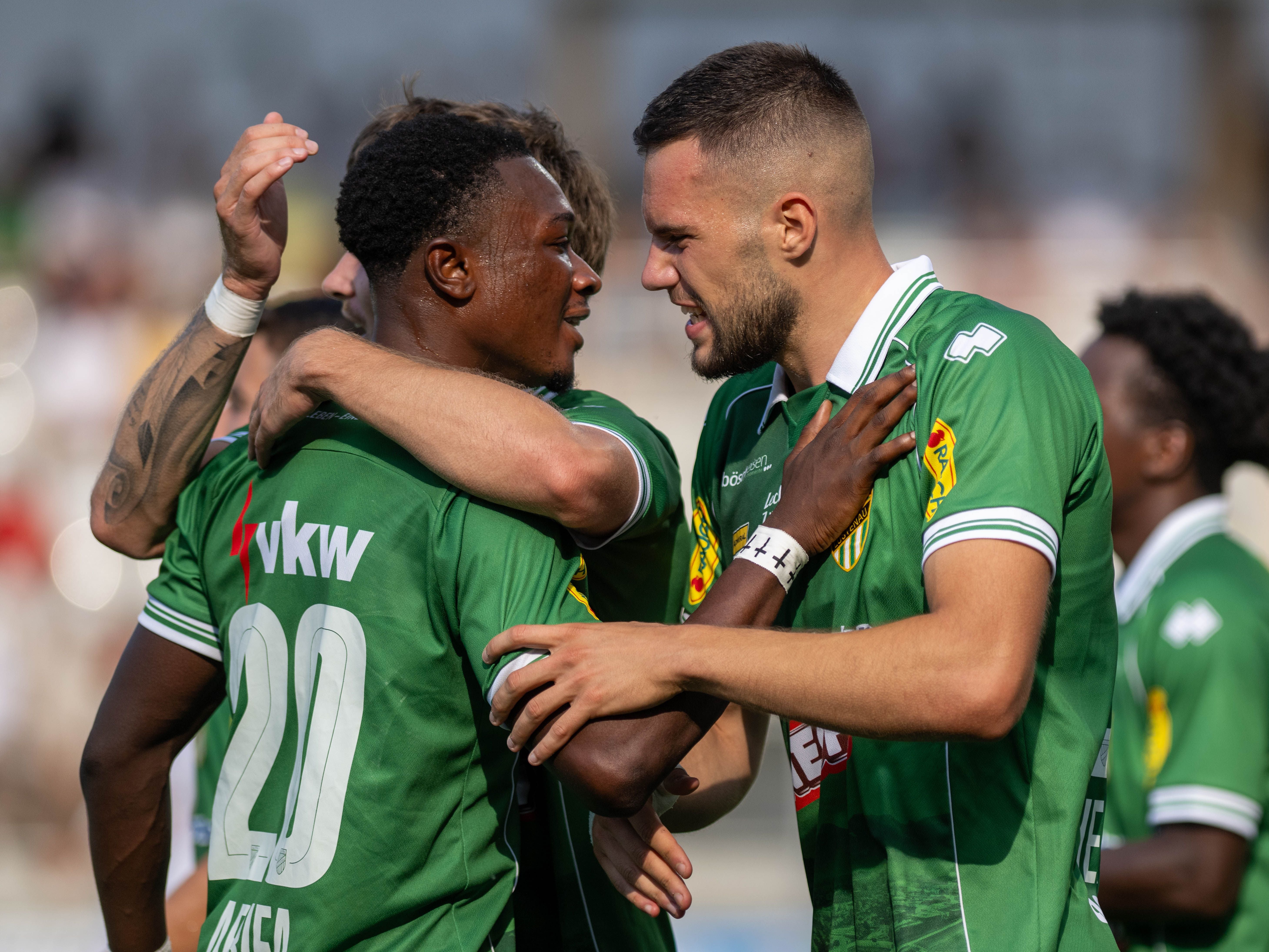 Zwei Fußballspieler im grünen Trikot jubeln nach einem Tor zusammen auf dem Spielfeld.