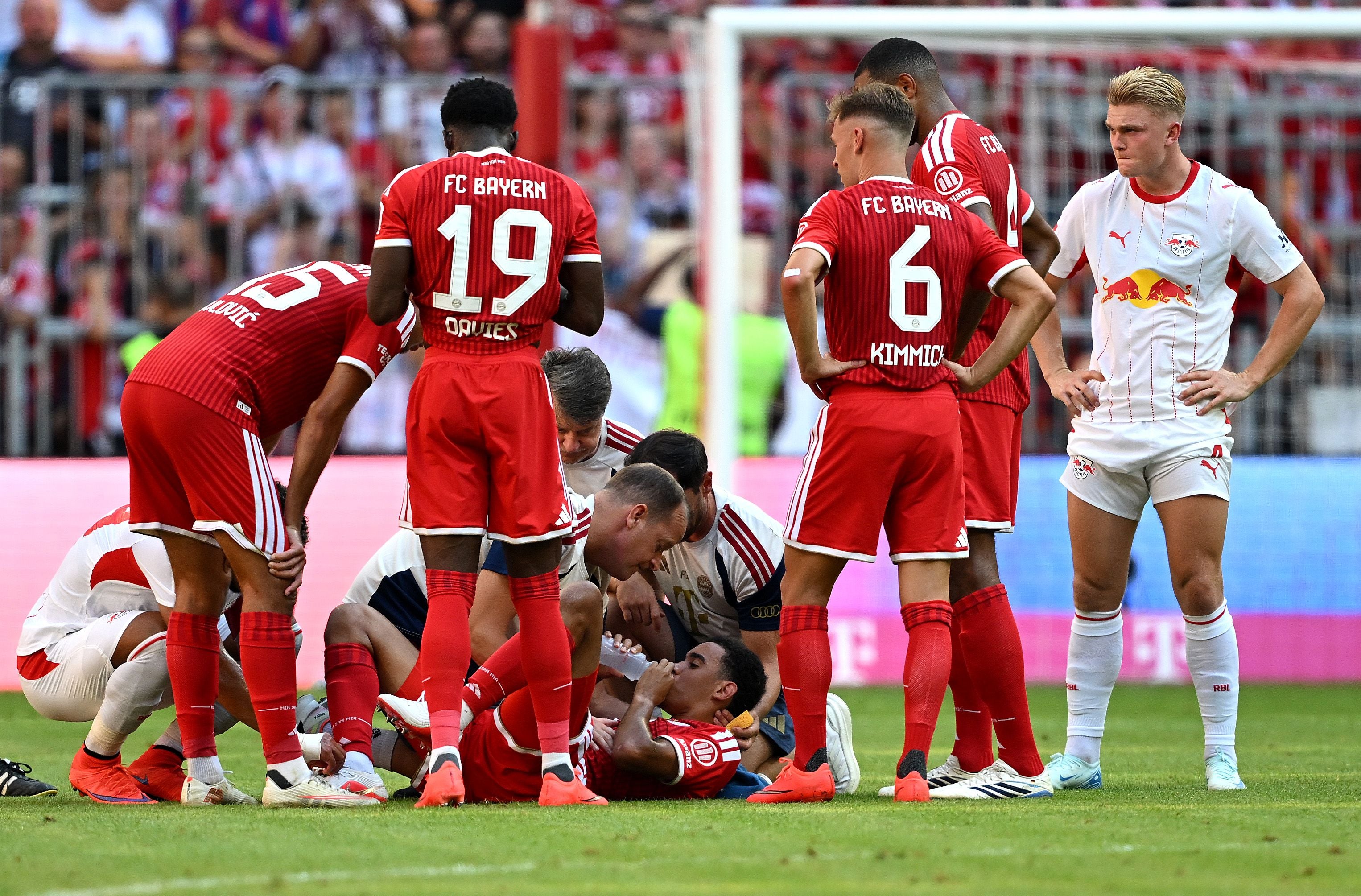 Ein verletzter Bayern-Spieler erhält medizinische Hilfe, umgeben von Teamkollegen und Gegnern.