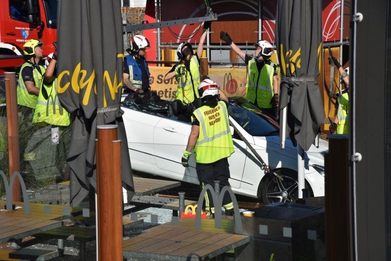 Mehrere Feuerwehrleute sichern ein weißes Auto im Gastgarten eines Fastfood-Restaurants.