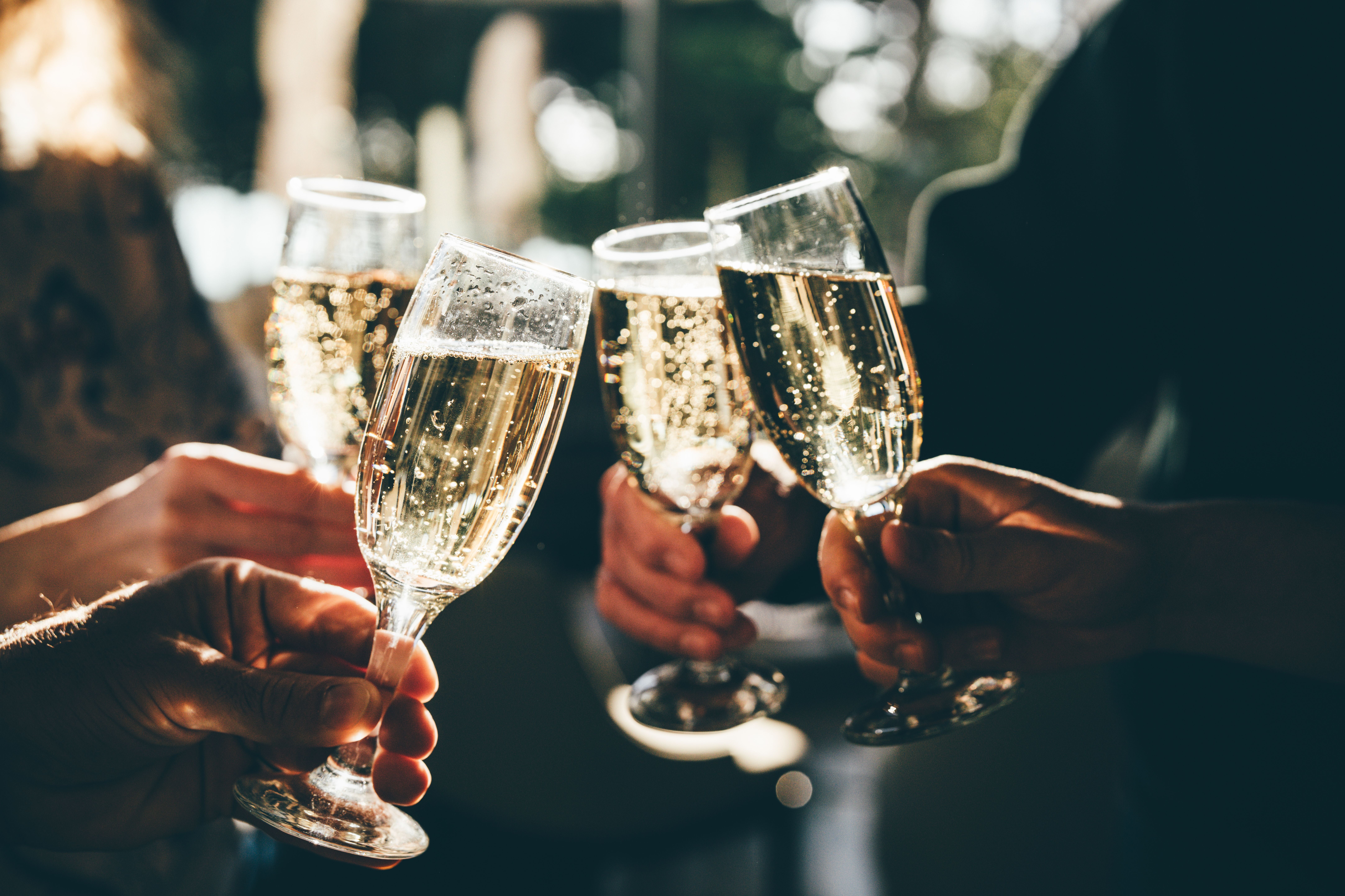 Vier Hände stoßen mit Champagnergläsern bei einer Feier an.