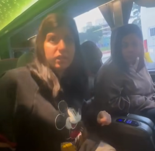 Zwei junge Frauen sitzen in einem Bus, eine trägt einen schwarzen Mickey-Mouse-Pullover.