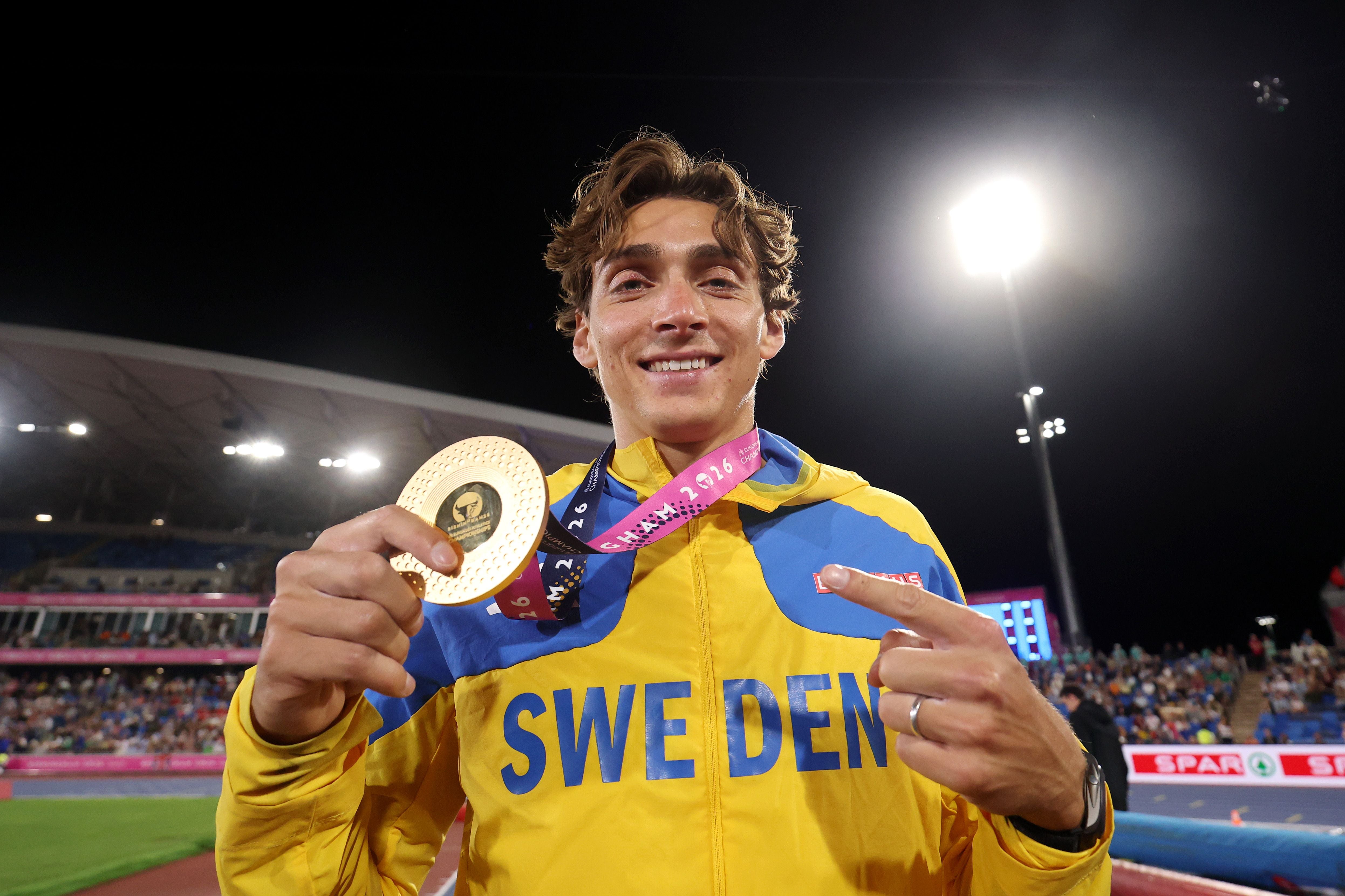 Ein Sportler im Schweden-Trikot hält lächelnd eine Goldmedaille im Stadion hoch.