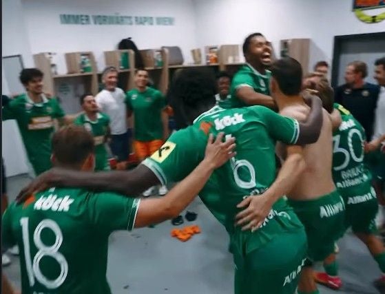 Mehrere Fußballspieler von Rapid feiern jubelnd in der Umkleidekabine.