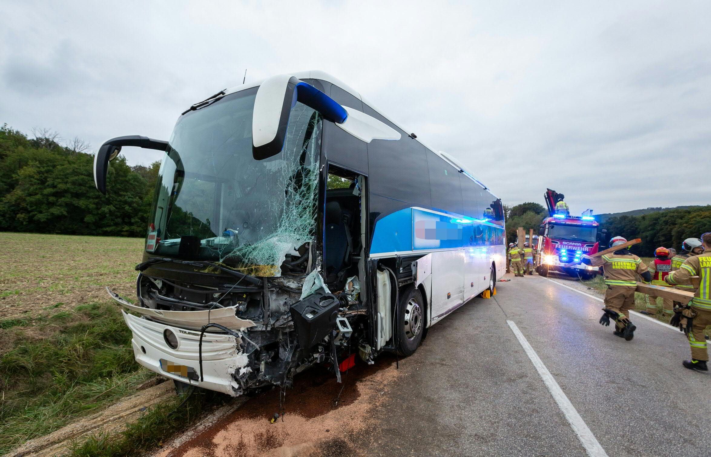 Ein Reisebus mit schwer beschädigter Front nach einem Unfall, Feuerwehrkräfte am Einsatzort.