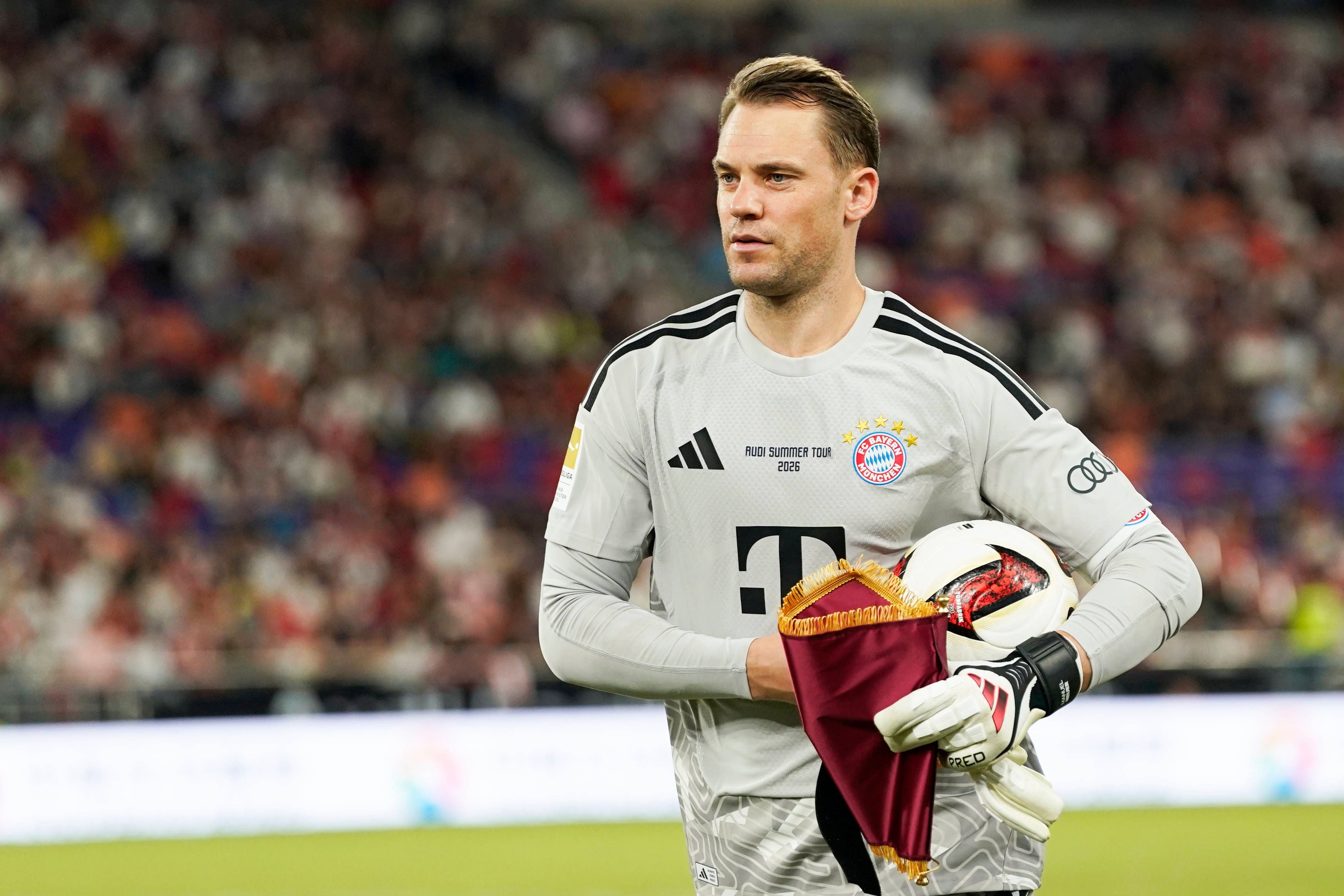Ein Torwart des FC Bayern München hält einen Fußball und eine Fahne im Stadion.