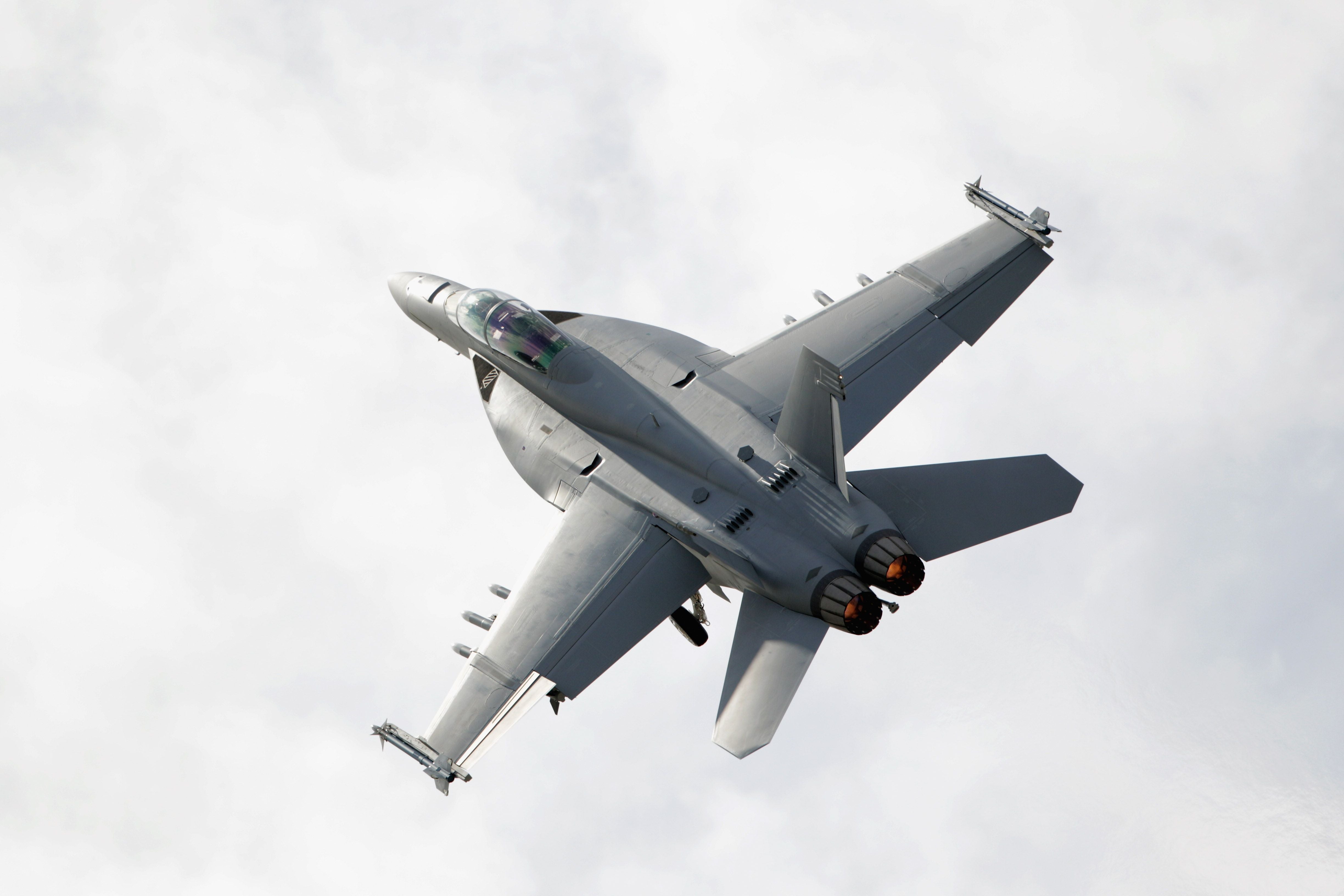 Ein F-18 Kampfjet startet mit Nachbrennern vor bewölktem Himmel.