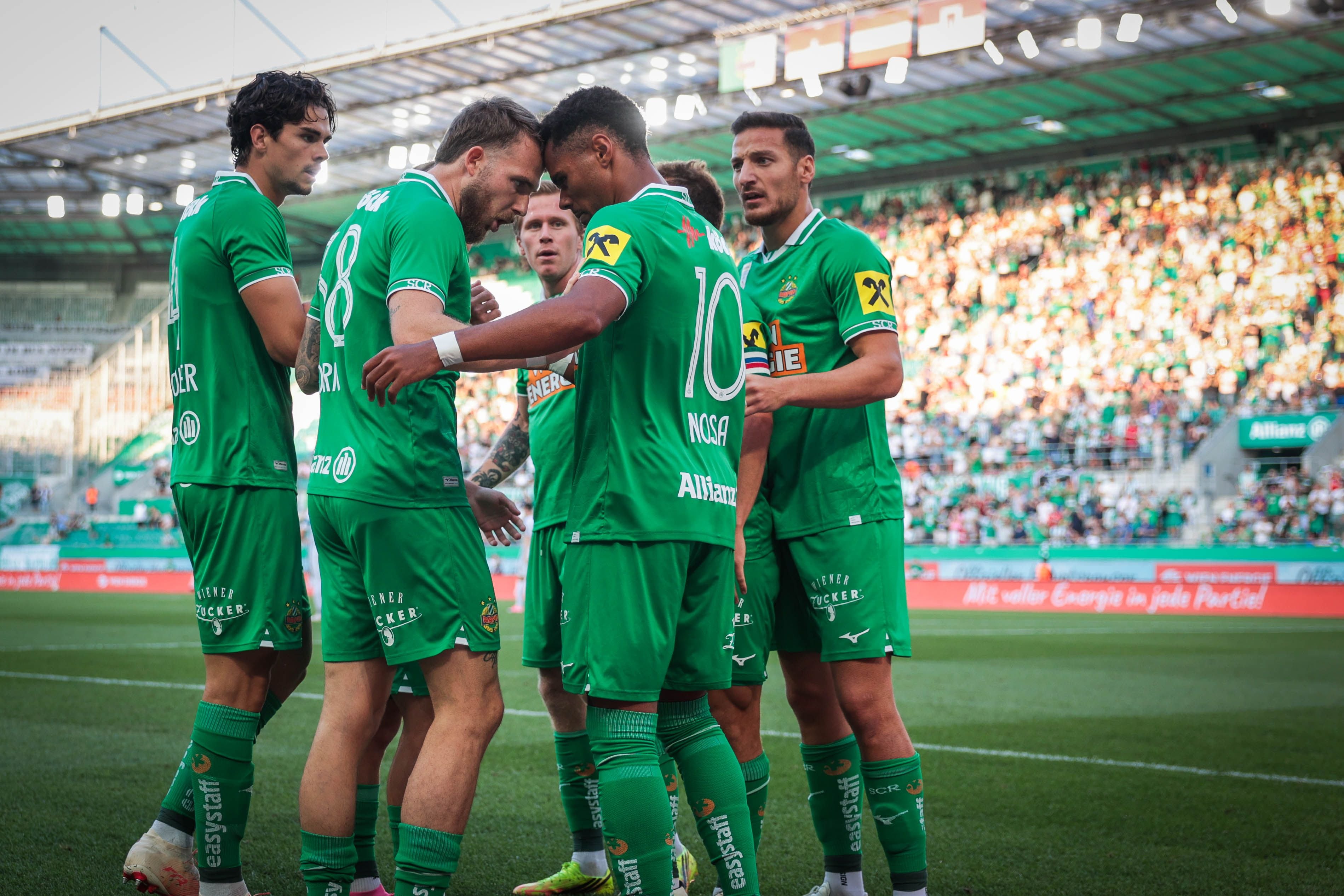 Mehrere Fußballspieler von Rapid Wien feiern gemeinsam ein Tor im Stadion.