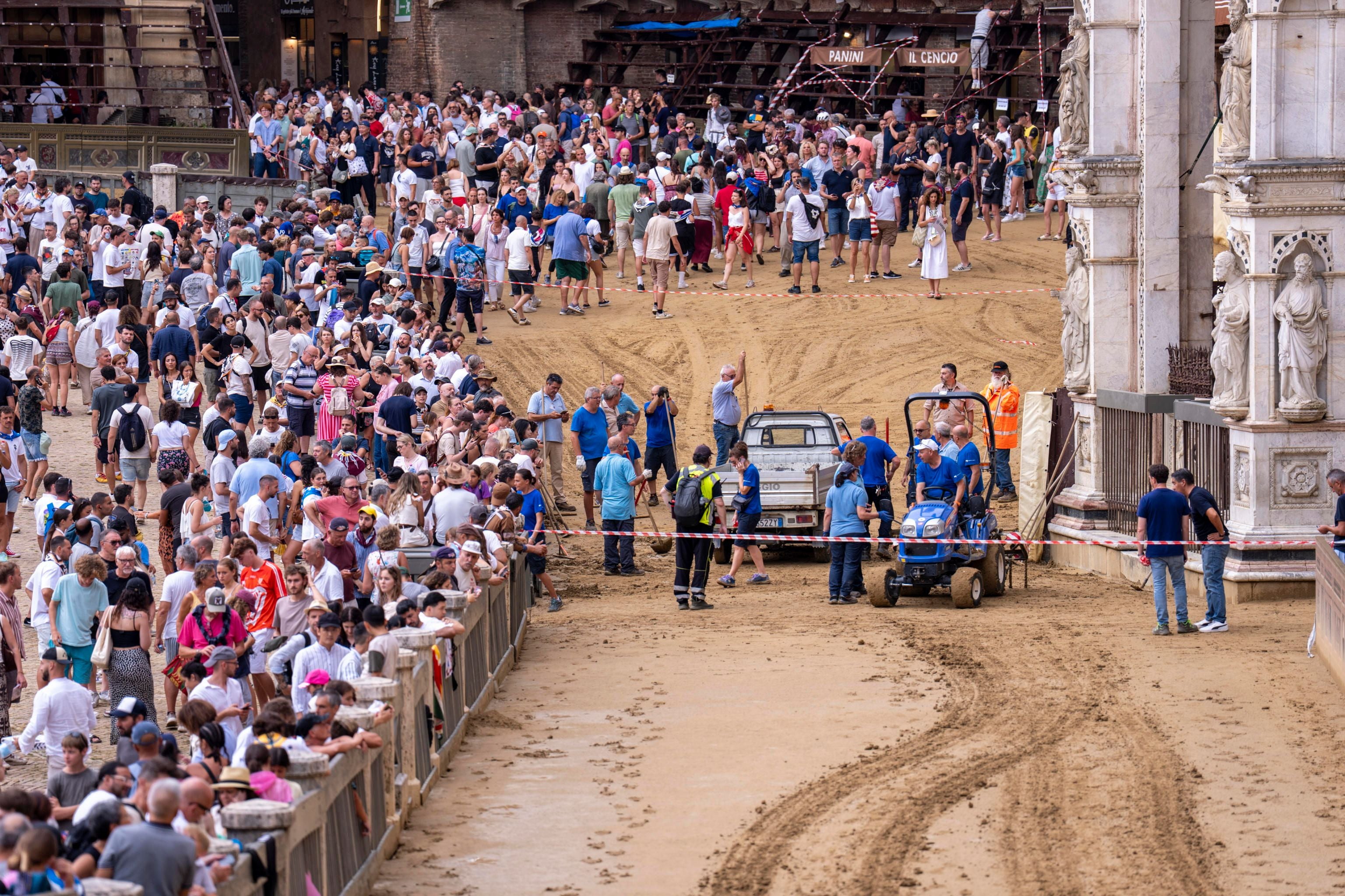 Menschenmenge am leeren, abgesperrten Sandrennplatz nach Verschiebung des Palio di Siena.