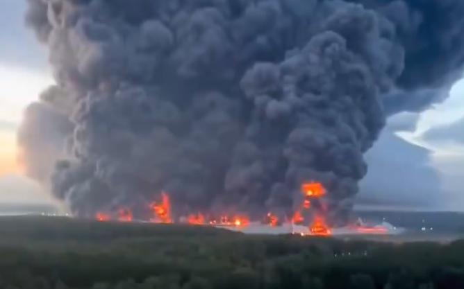 Großbrand mit meterhohen Flammen und dichter schwarzer Rauchwolke über einem Industriegebiet.