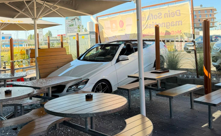 Ein weißes Auto ist in den Außenbereich eines Cafés mit Tischen und Bänken gefahren.
