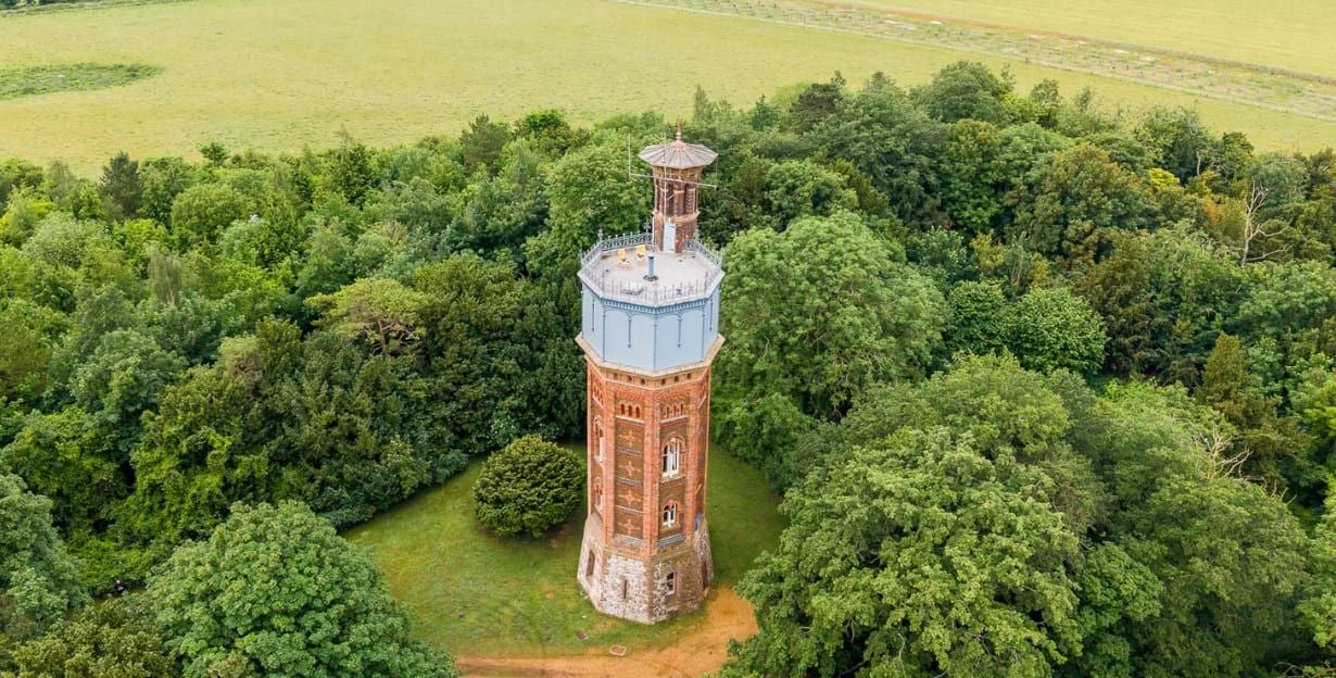 Backsteinturm steht von Bäumen umgeben auf einer Lichtung neben einem großen Feld.