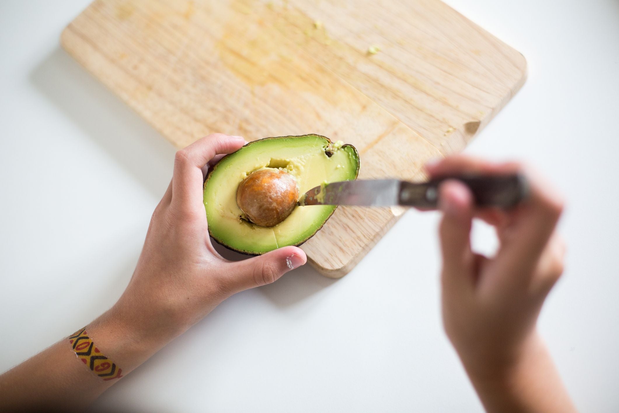 Eine Hand hält eine halbierte Avocado, während die andere mit einem Messer arbeitet.