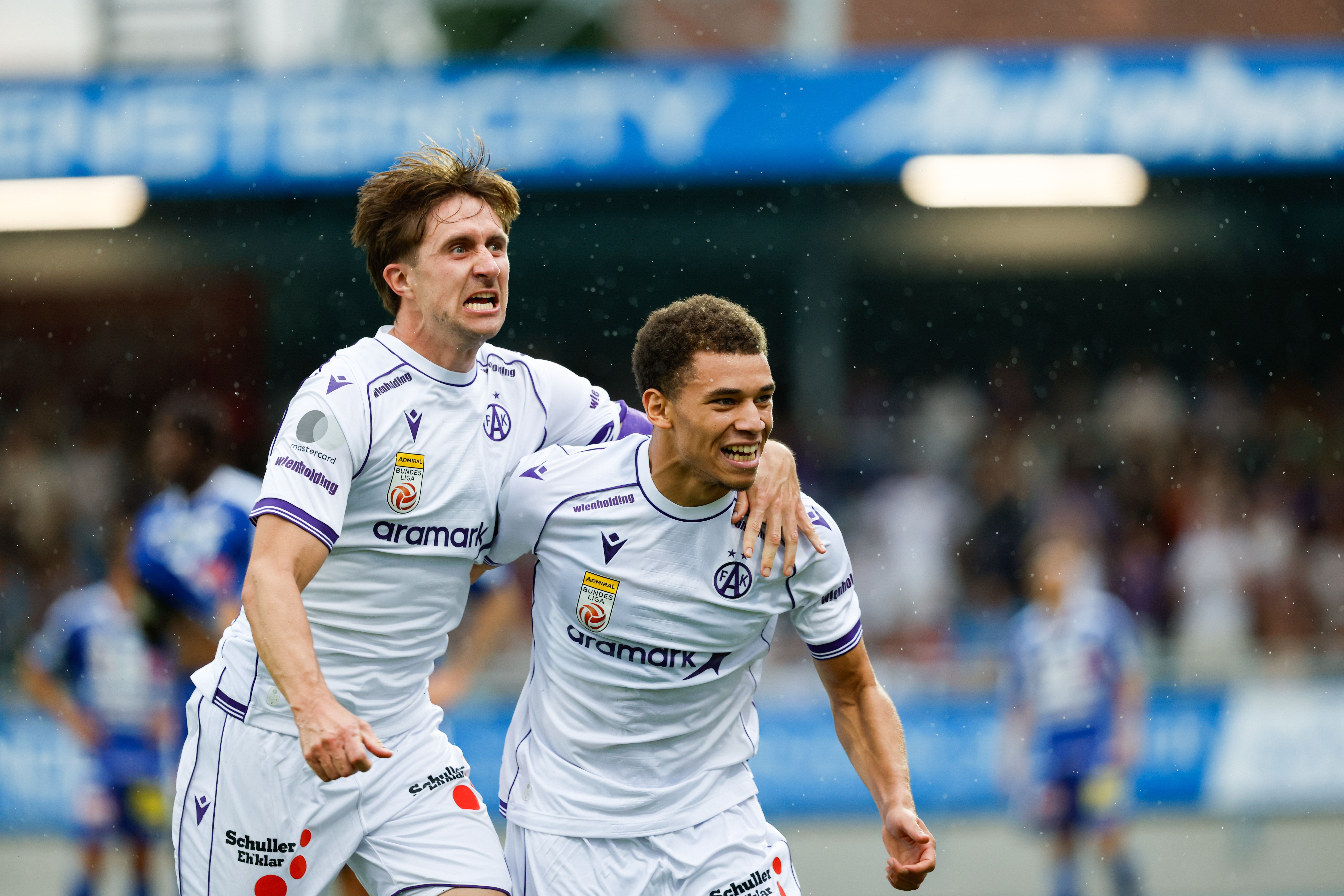 Zwei Austria-Wien-Spieler jubeln auf dem Fußballfeld im weißen Trikot.