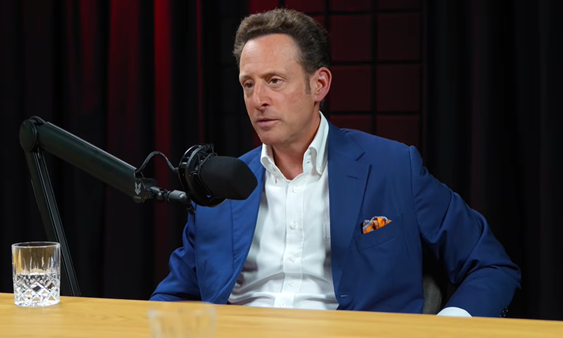 Ein Mann im blauen Anzug spricht in ein Mikrofon während eines Podcasts.
