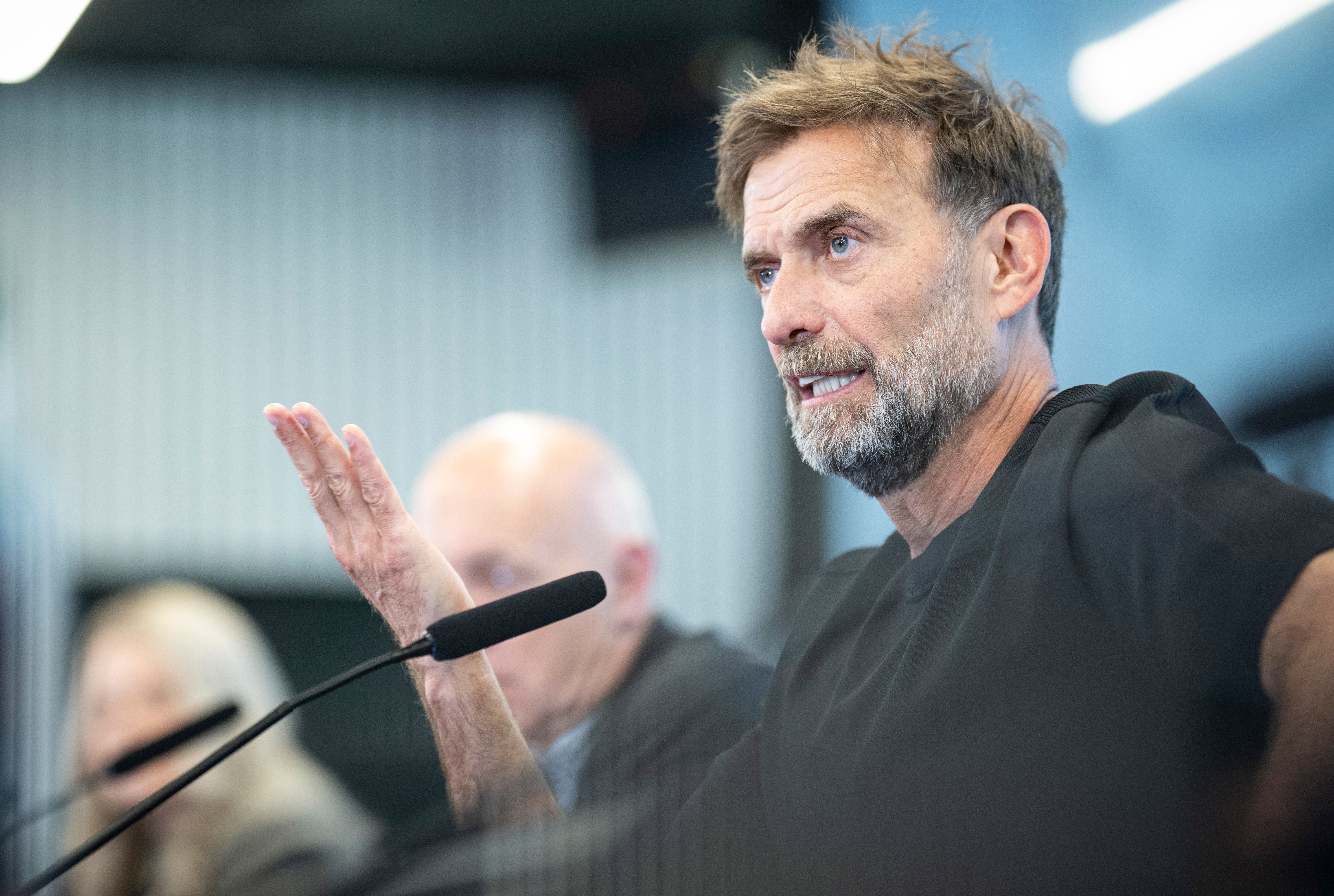 Ein Mann mit Bart spricht bei einer Pressekonferenz und gestikuliert mit der Hand.
