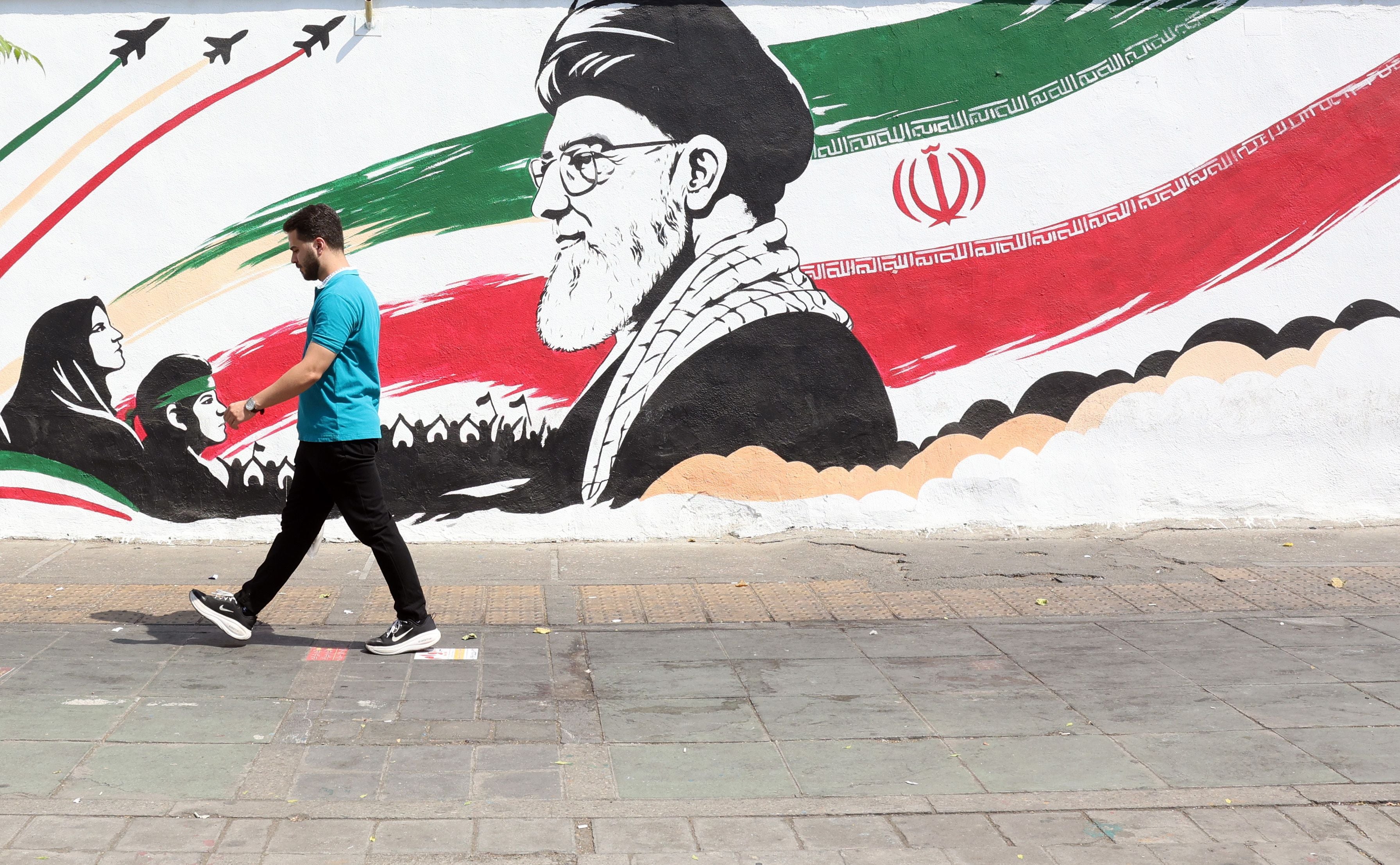 Ein Mann geht an einem Wandgemälde mit iranischer Flagge und Porträts vorbei.
