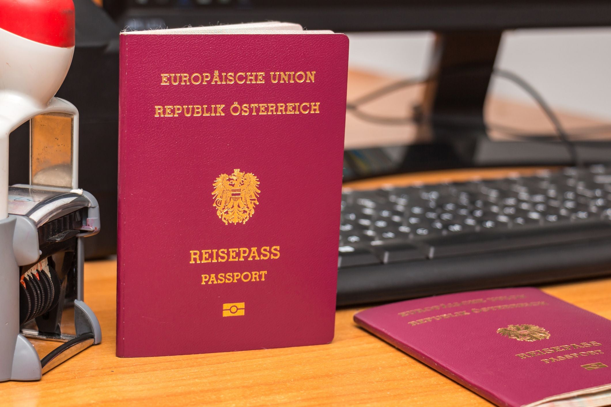 Österreichischer Reisepass steht auf einem Schreibtisch vor einer Tastatur und einem Stempelgerät.