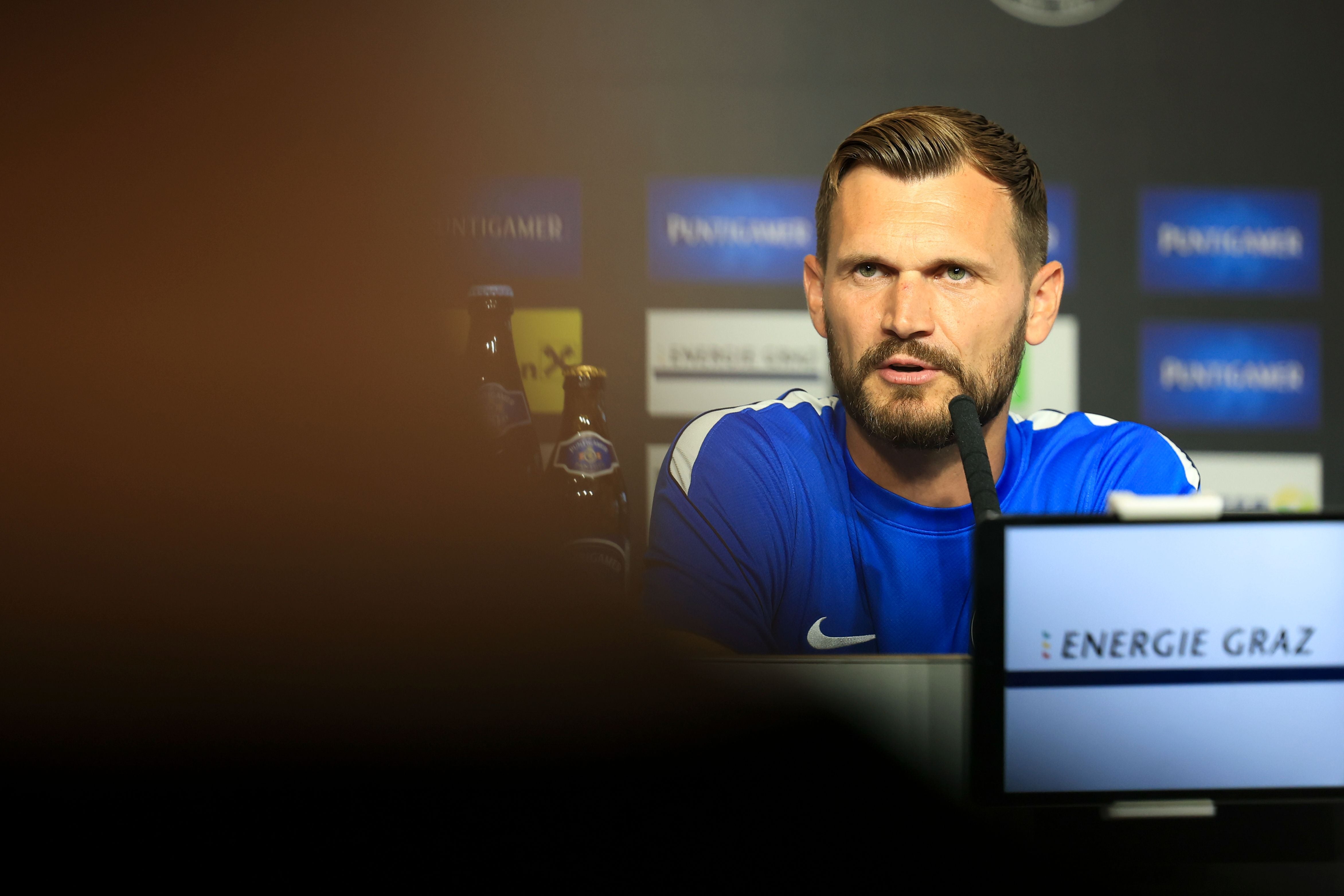 Sturm-Trainer Fabio Ingolitsch spricht bei einer Pressekonferenz vor Sponsorenwänden ins Mikrofon.