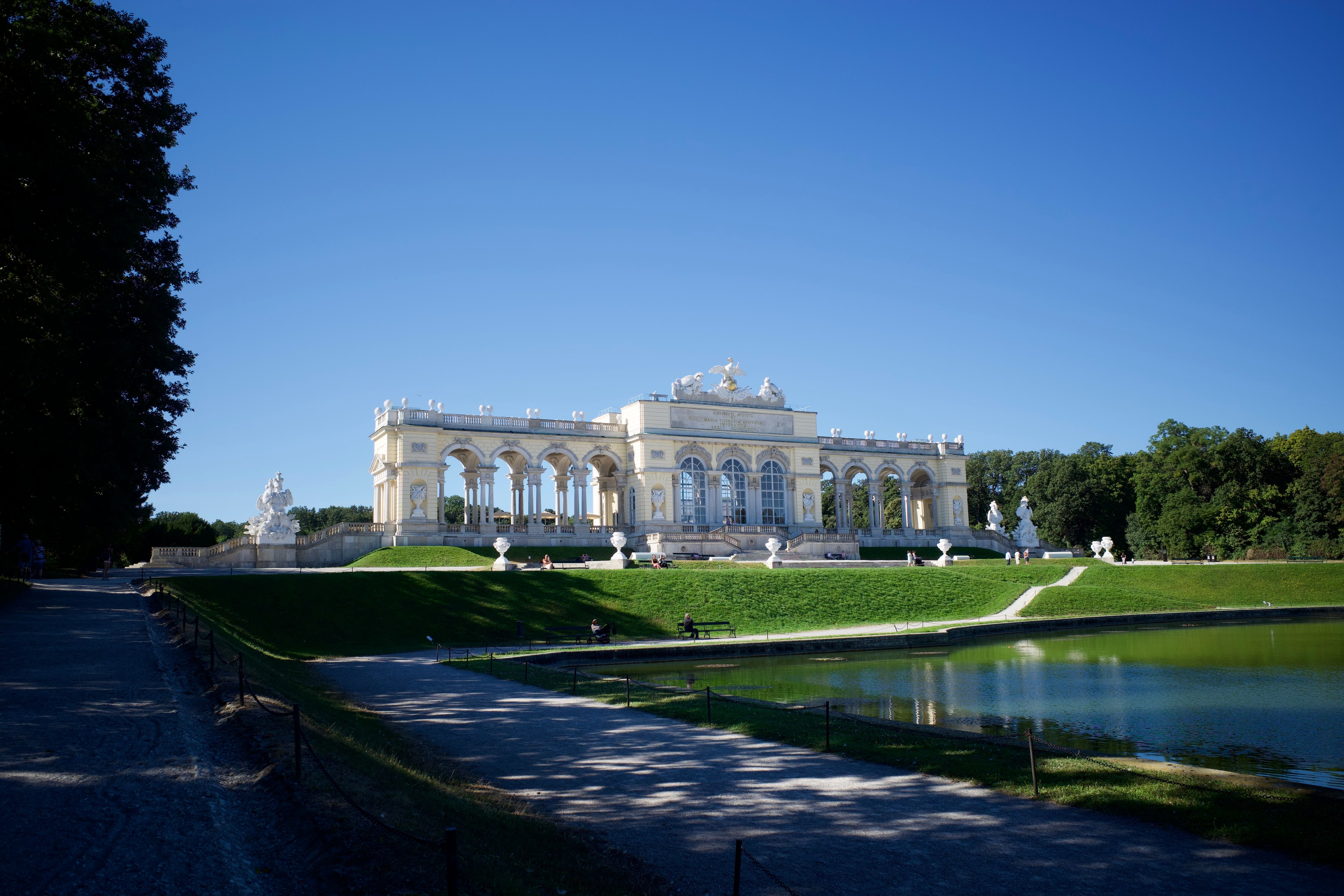 Die Gloriette im Schlosspark Schönbrunn in Wien spiegelt sich im Teich, sonniger Himmel.