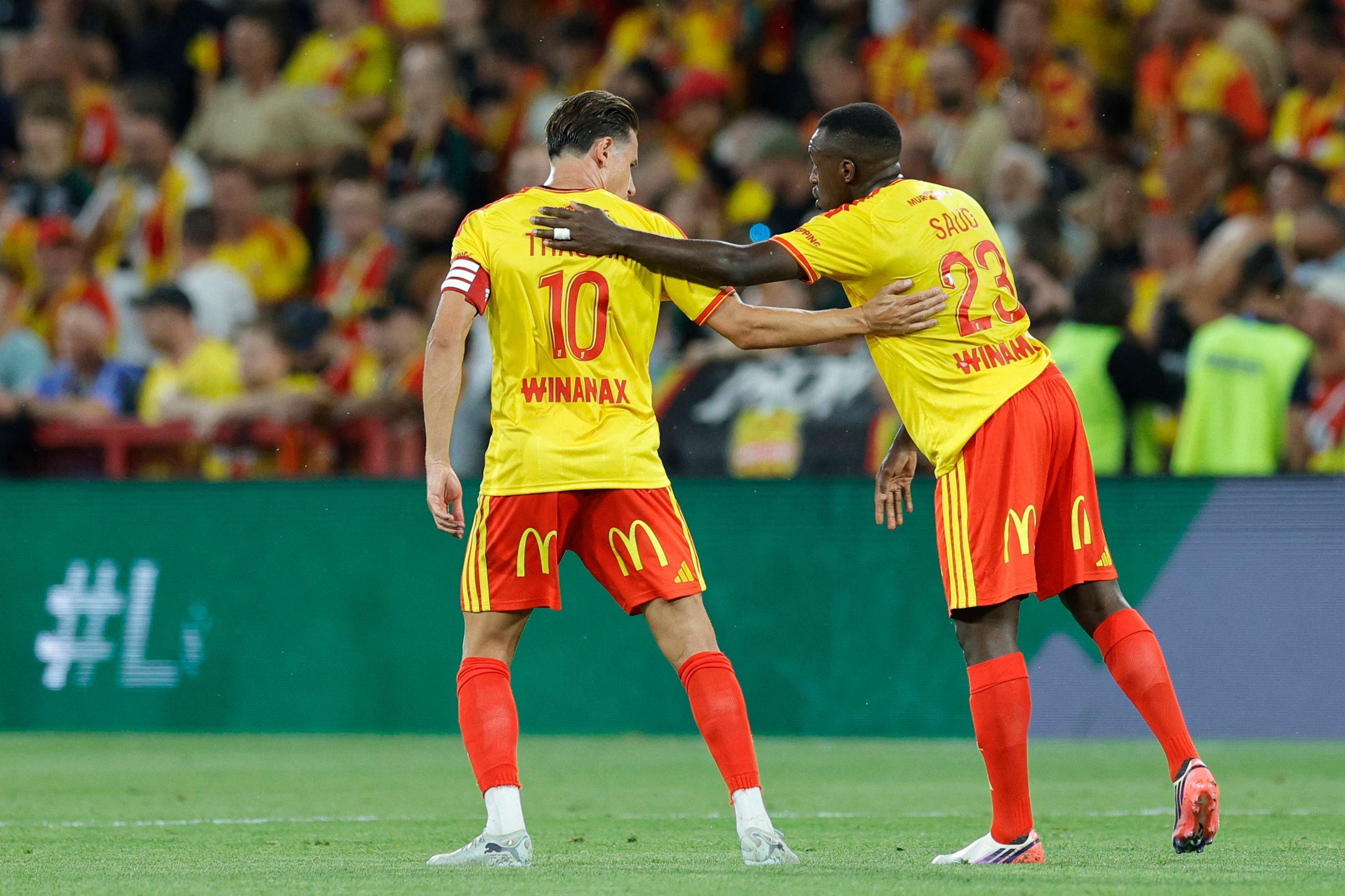 Zwei Fußballspieler von RC Lens feiern gemeinsam ein Tor auf dem Spielfeld.