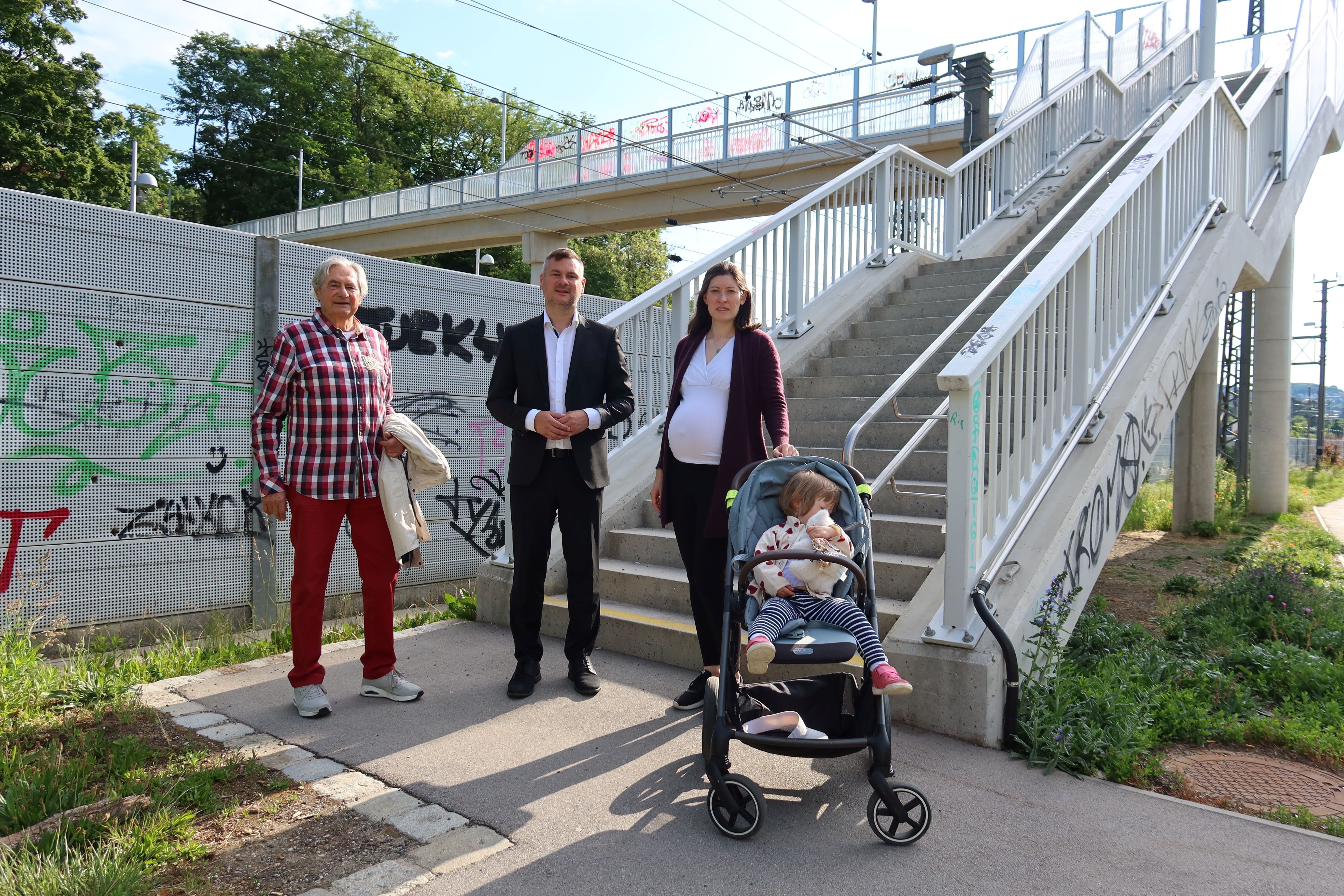 Drei Erwachsene und ein Kind im Kinderwagen stehen vor einer Treppe an der Loudonbrücke.