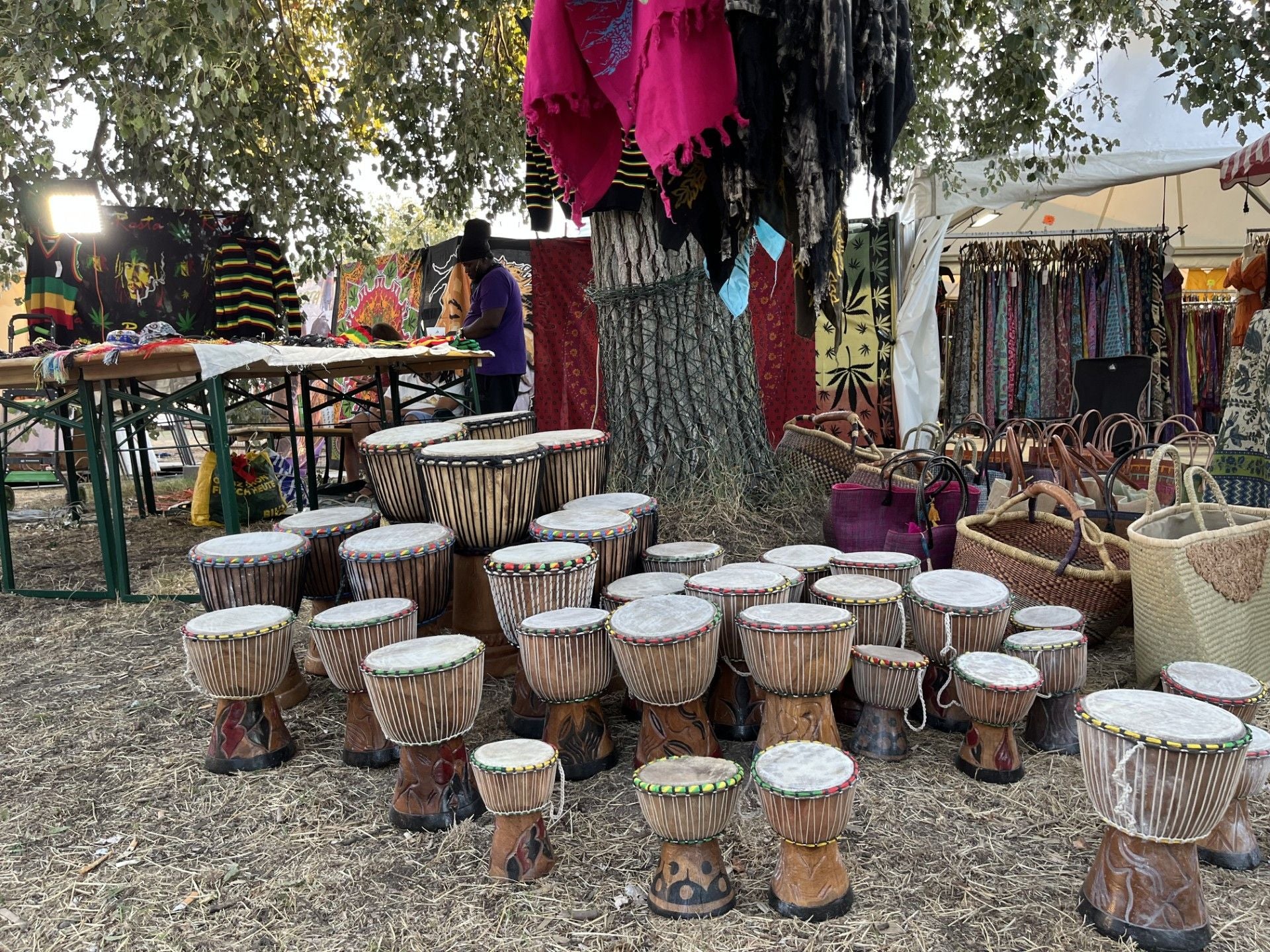 Viele Djembe-Trommeln und Korbtaschen stehen bei einem Afrika-Markt im Freien ausgestellt.