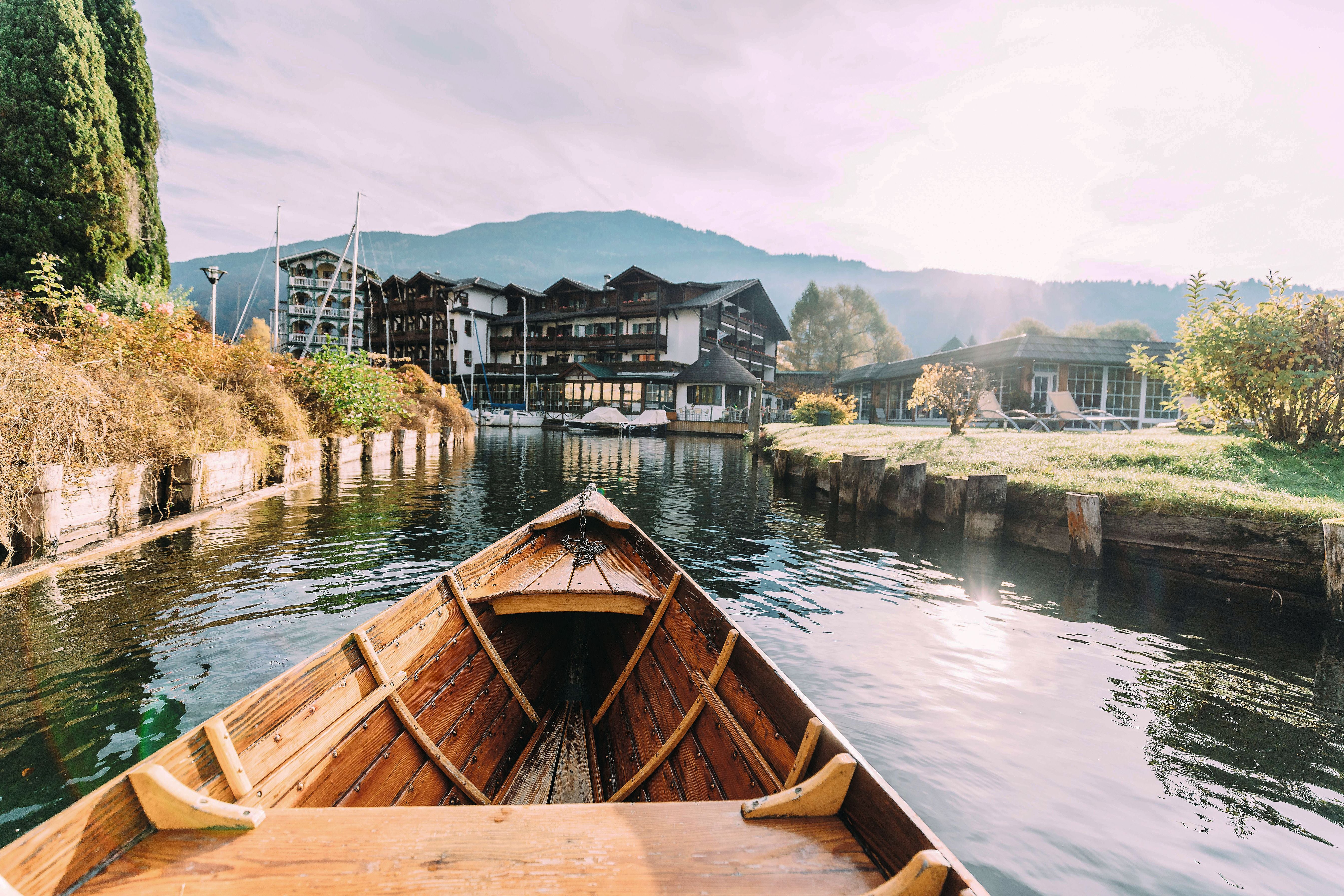 Blick aus einem Holzboot auf ein Ufer mit Hotelgebäude und grüner Landschaft im Sonnenlicht.