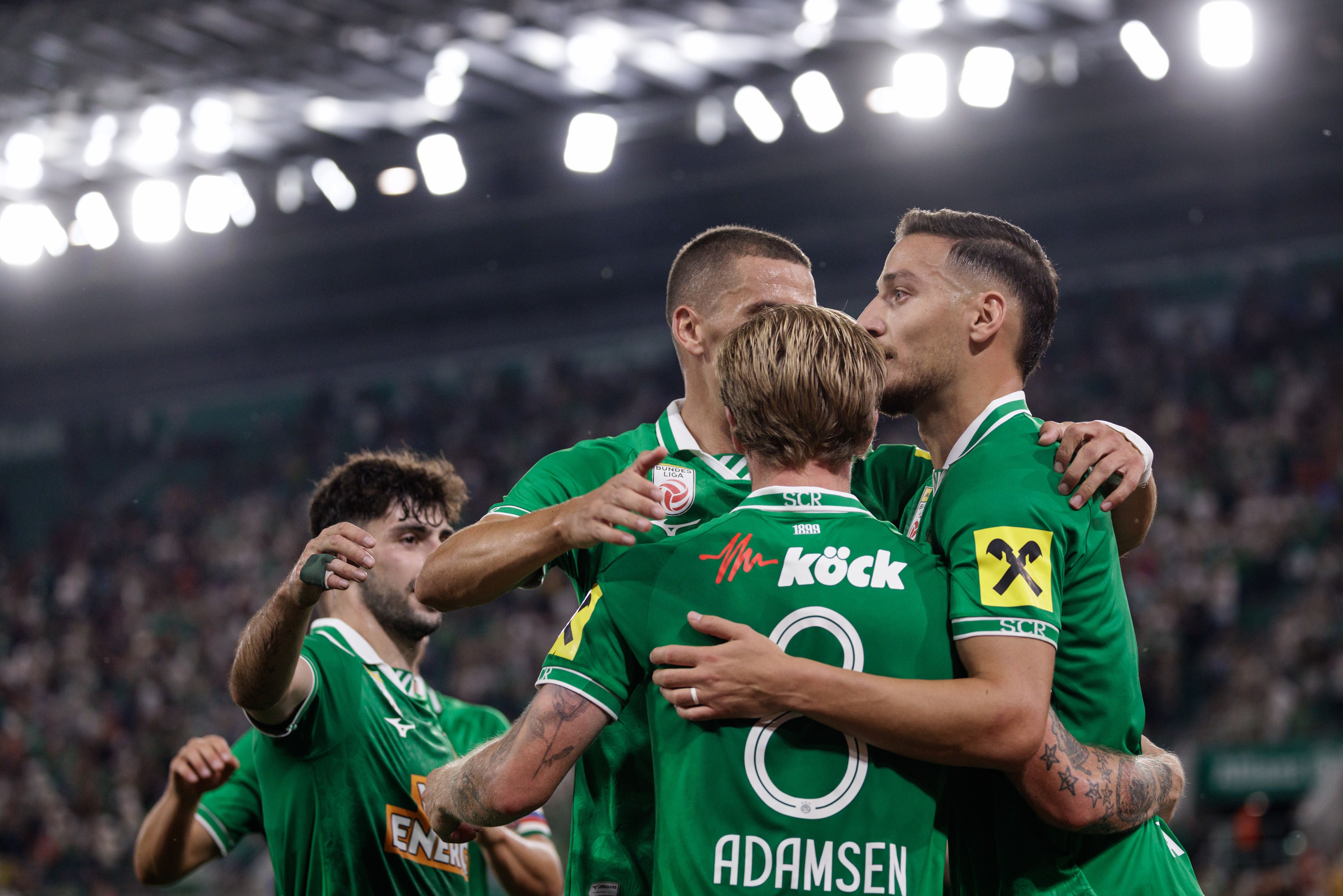 Rapid-Spieler jubeln nach einem Tor, umarmen sich im Stadion in grünen Trikots.